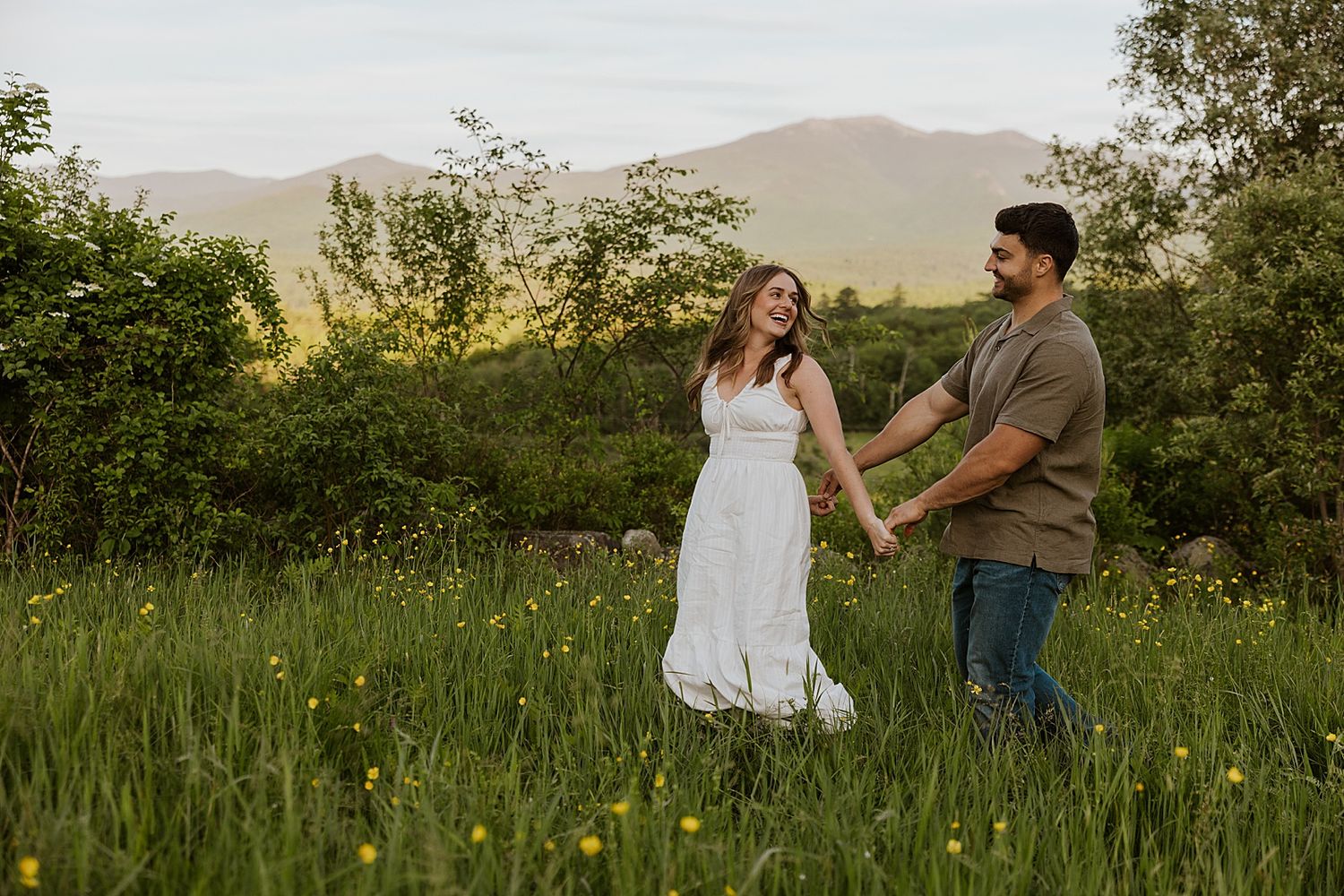 New Hampshire couple walking through a wildflower field taking golden hour engagement photos