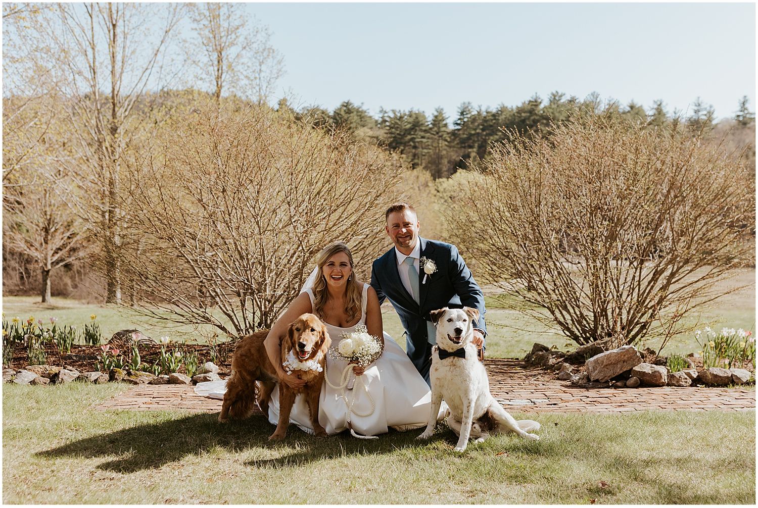 A couple poses with their dogs in a scenic spring field.