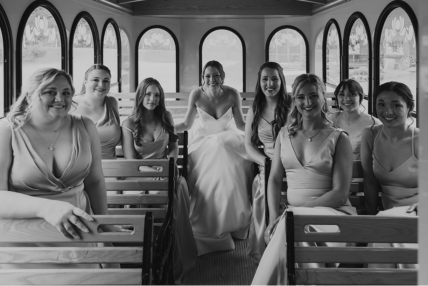 Wedding party members seated in rows on wooden benches in a dimly lit venue.