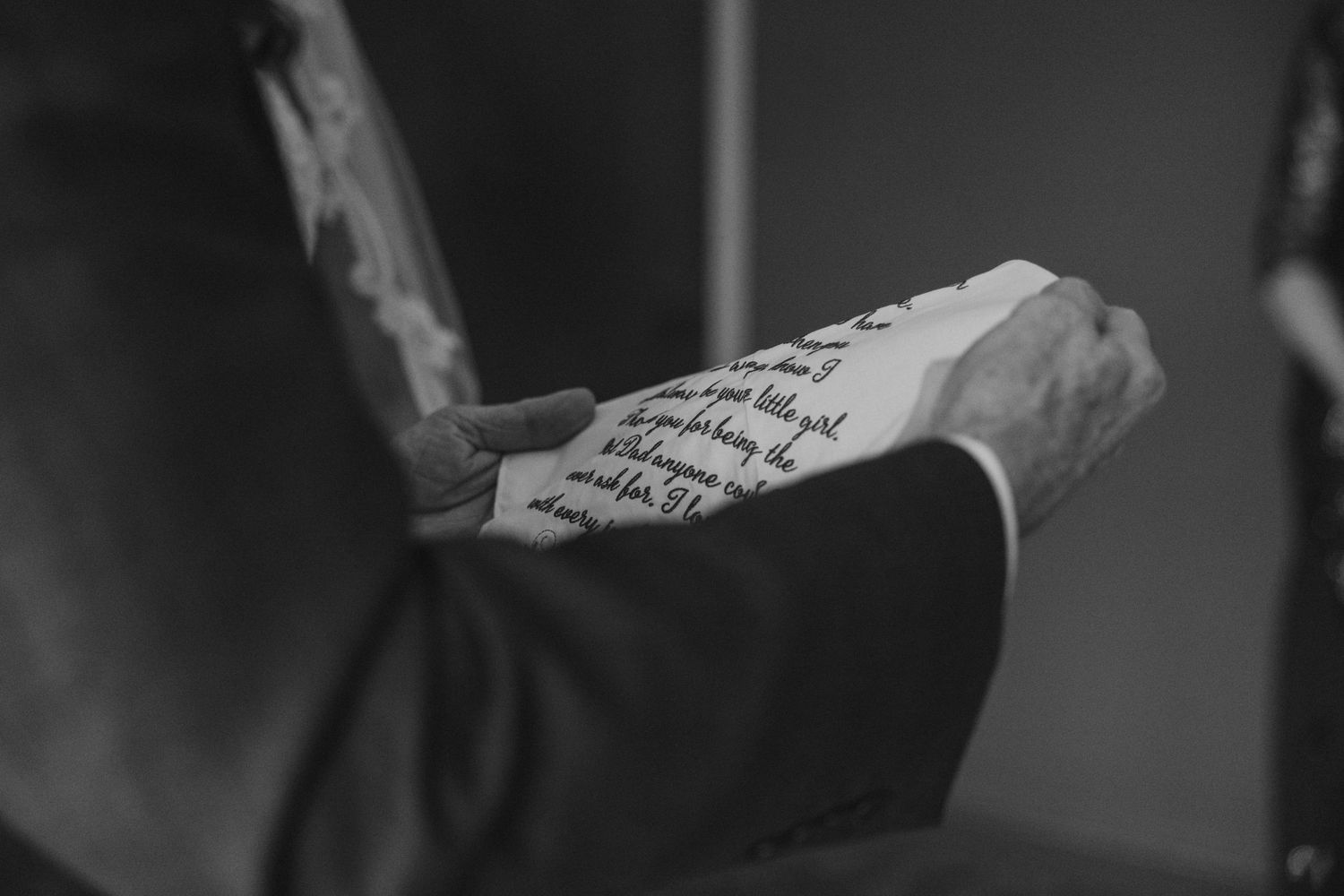 Black and white close-up of hands holding handwritten text on paper.