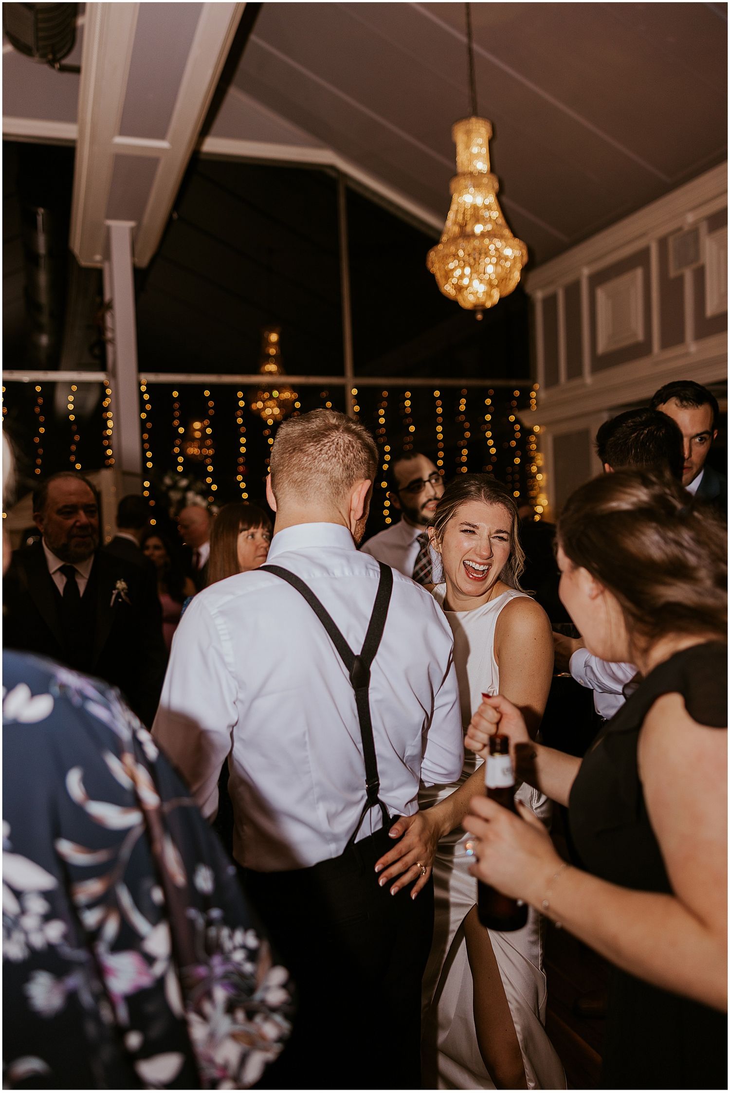 Wedding guests dancing and celebrating on a dark dance floor with string lights overhead.