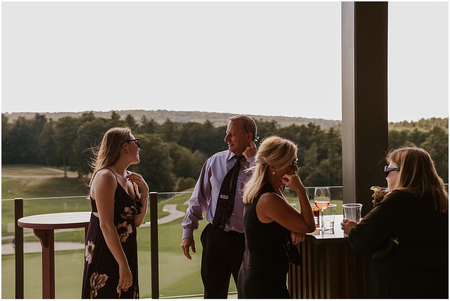 Silhouettes of wedding guests enjoying sunset views from a covered outdoor venue.
