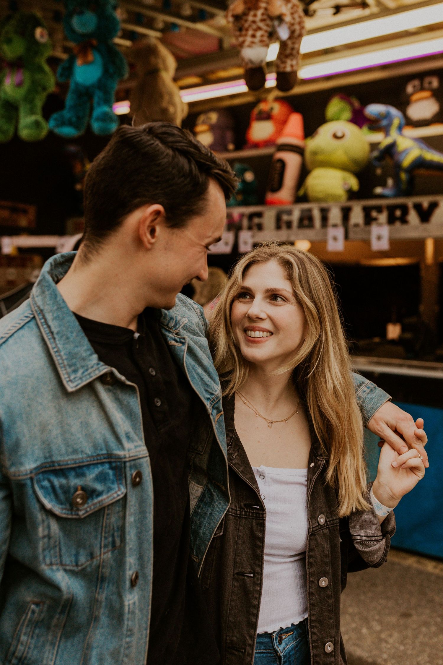 Couple laughing together at a carnival game booth with neon lights.