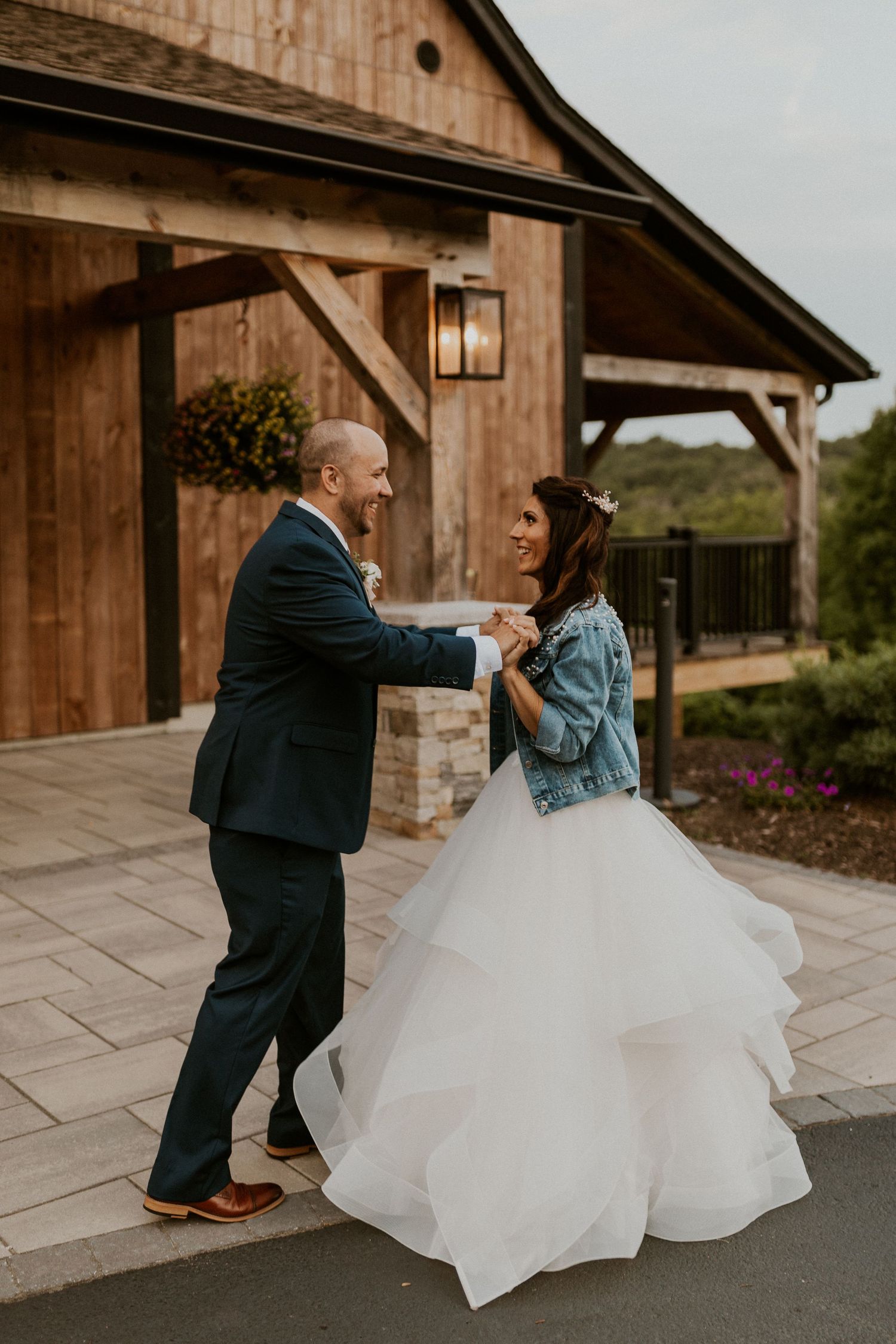 Dancing couple in wedding attire twirl outside a rustic wooden barn venue.