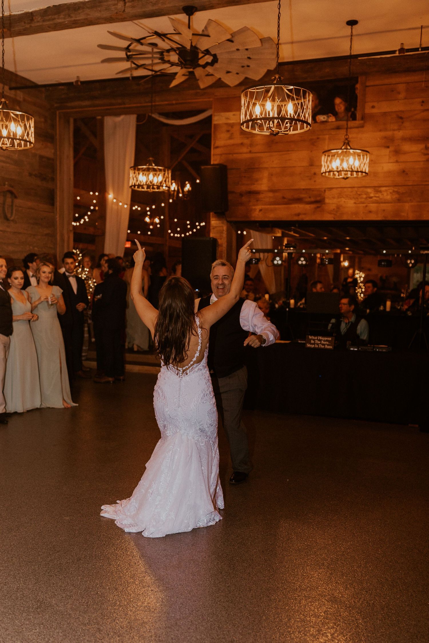 Wedding reception dance floor with guests celebrating under warm chandelier lighting.