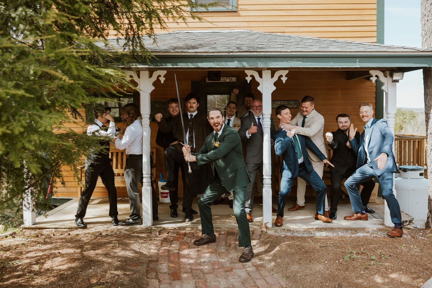 Groomsmen playfully posing and dancing outside a rustic wooden building during a wedding celebration.