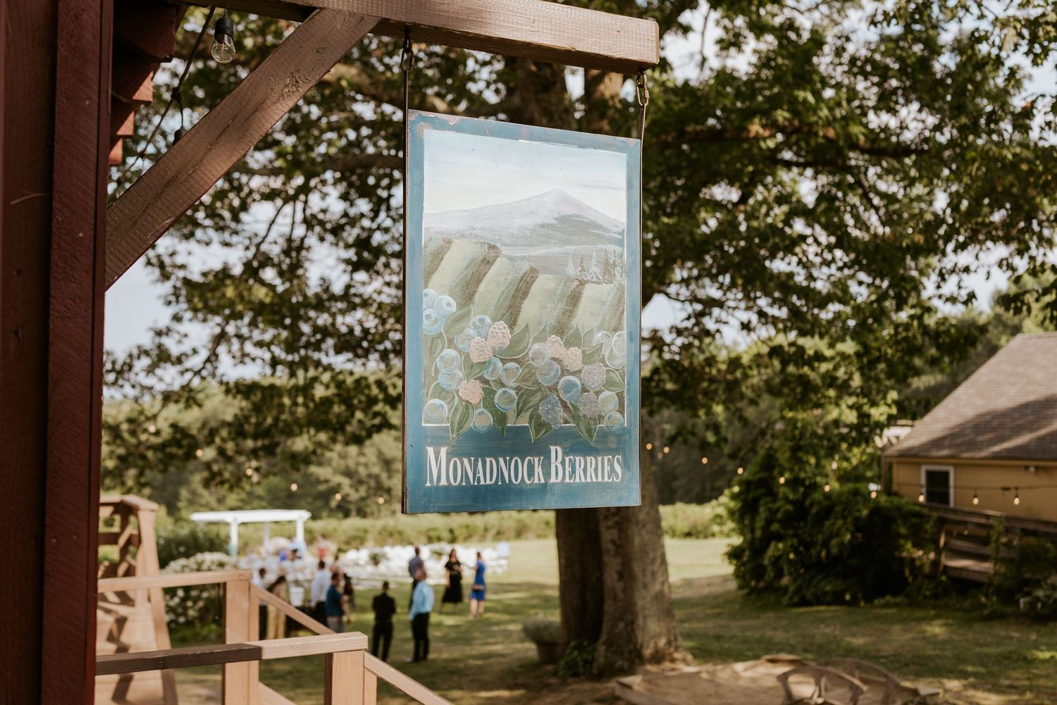 Monadnock Berries vintage style sign hanging under wooden pergola with scenic green outdoor wedding venue in background.