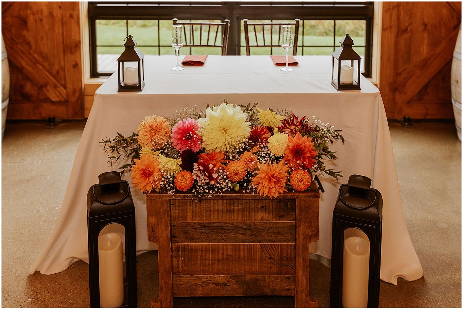 Rustic wedding reception tables decorated with orange and pink floral centerpieces and lantern accents.