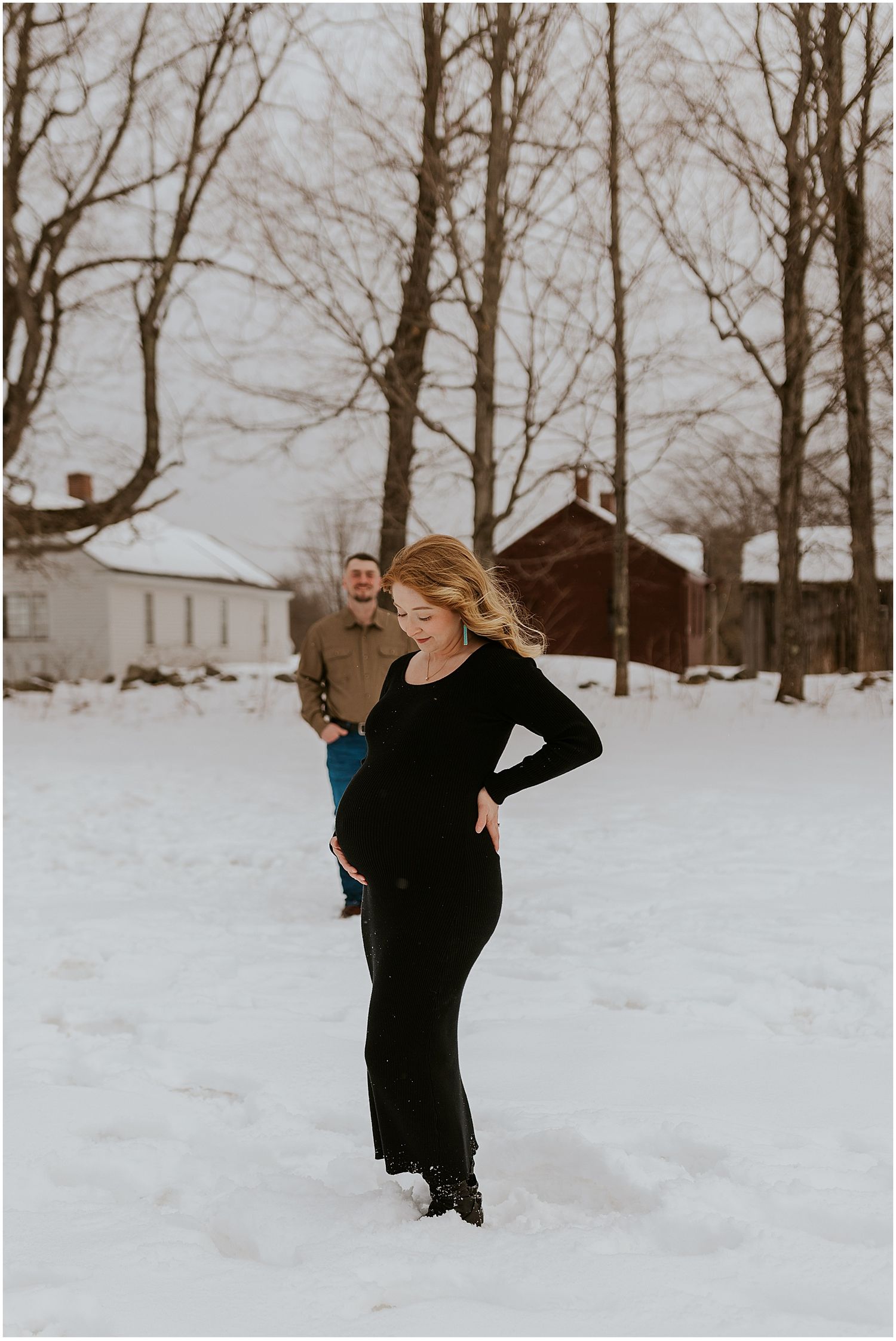 A playful winter engagement photoshoot with a couple frolicking in the snow against a backdrop of bare trees.