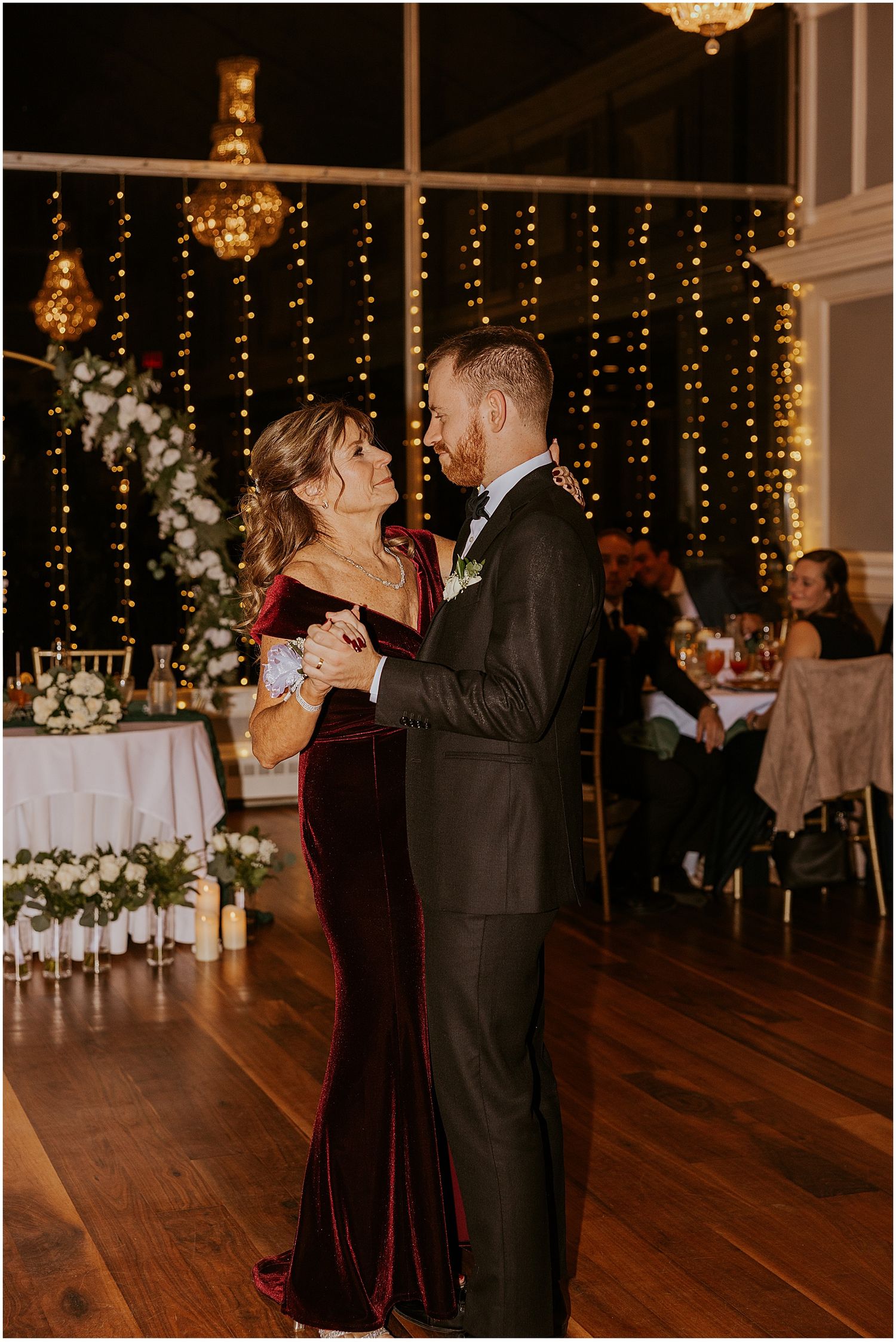Couples slow dancing at a wedding reception with string lights and chandeliers.