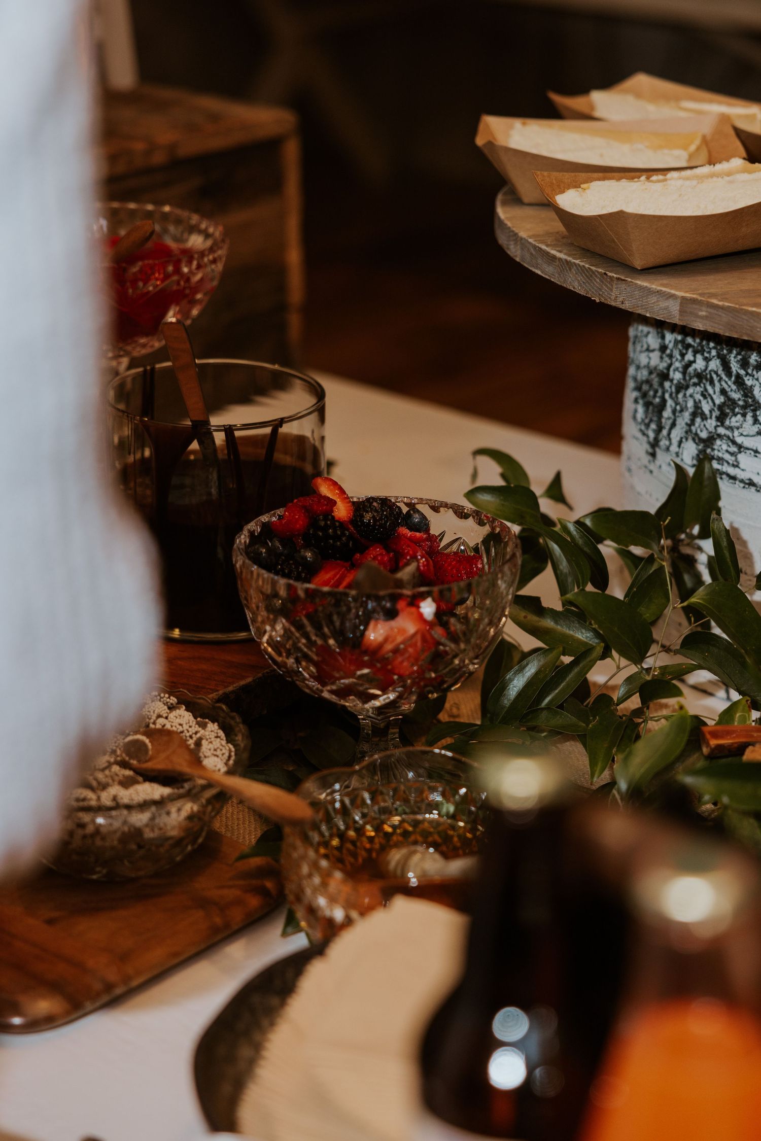 Wedding reception table detail with crystal bowls of berries and greenery decorations.