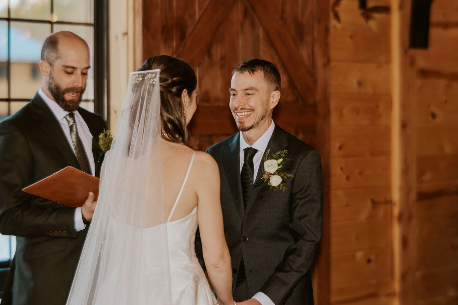 A wedding ceremony takes place inside a rustic wooden barn venue with warm natural lighting.