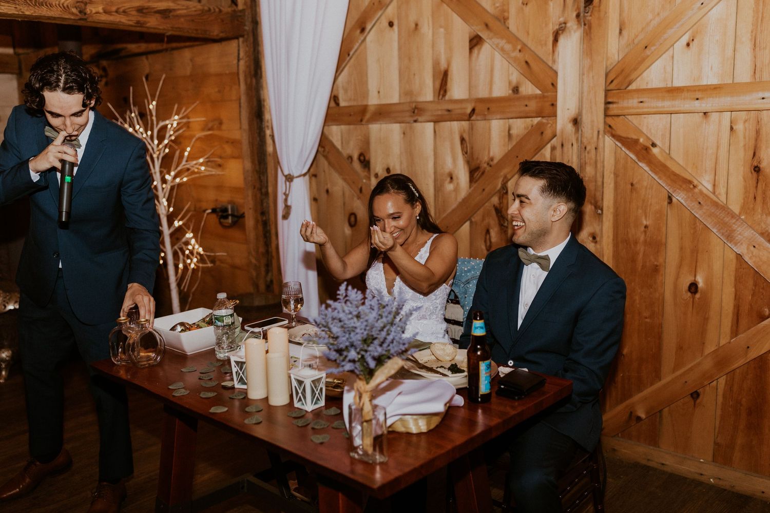 Wedding reception dinner in a rustic barn venue with elegant table settings and natural wood decor.