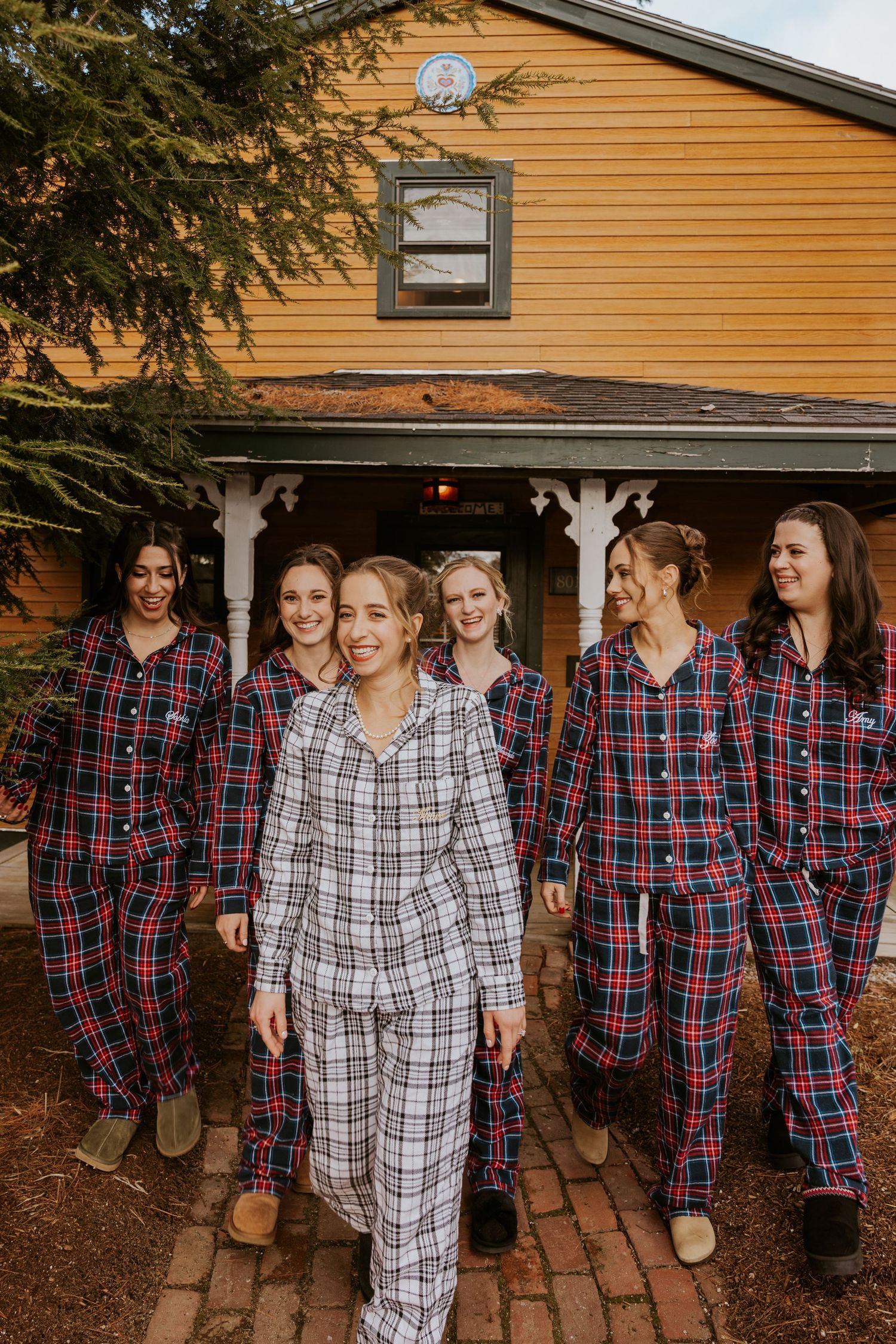 Bride leading bridesmaids in matching plaid pajamas outside a rustic venue during wedding morning.