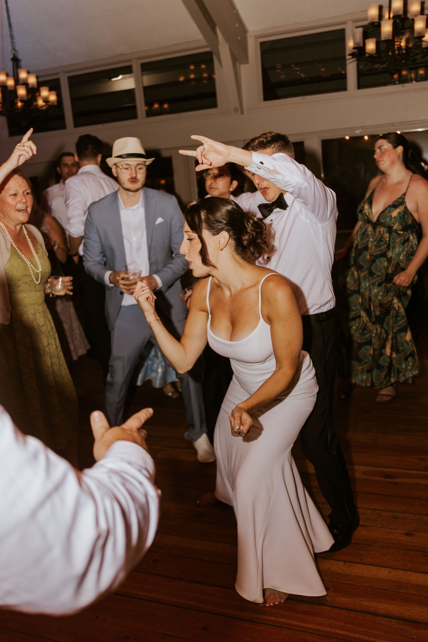 Bride dancing energetically with guests on crowded wedding reception dance floor.