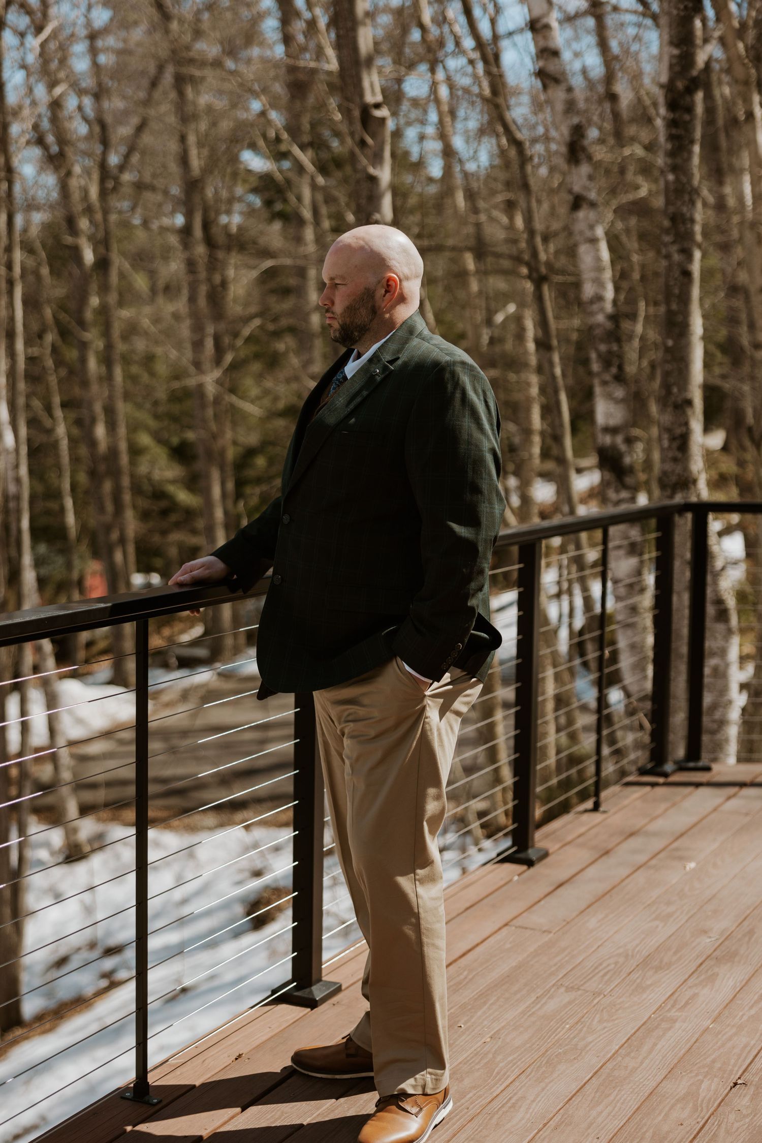 A couple shares a romantic moment on a snow-covered wooden deck surrounded by winter trees.