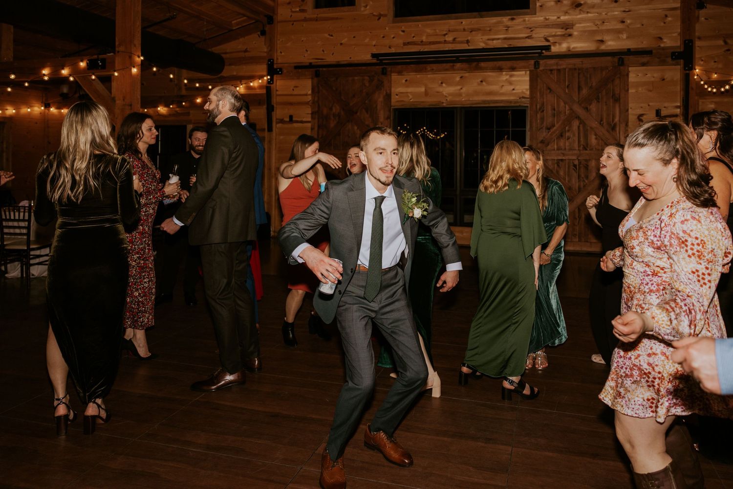 Guests enjoying a lively dance party at a rustic barn wedding reception with wooden beams and ambient lighting.