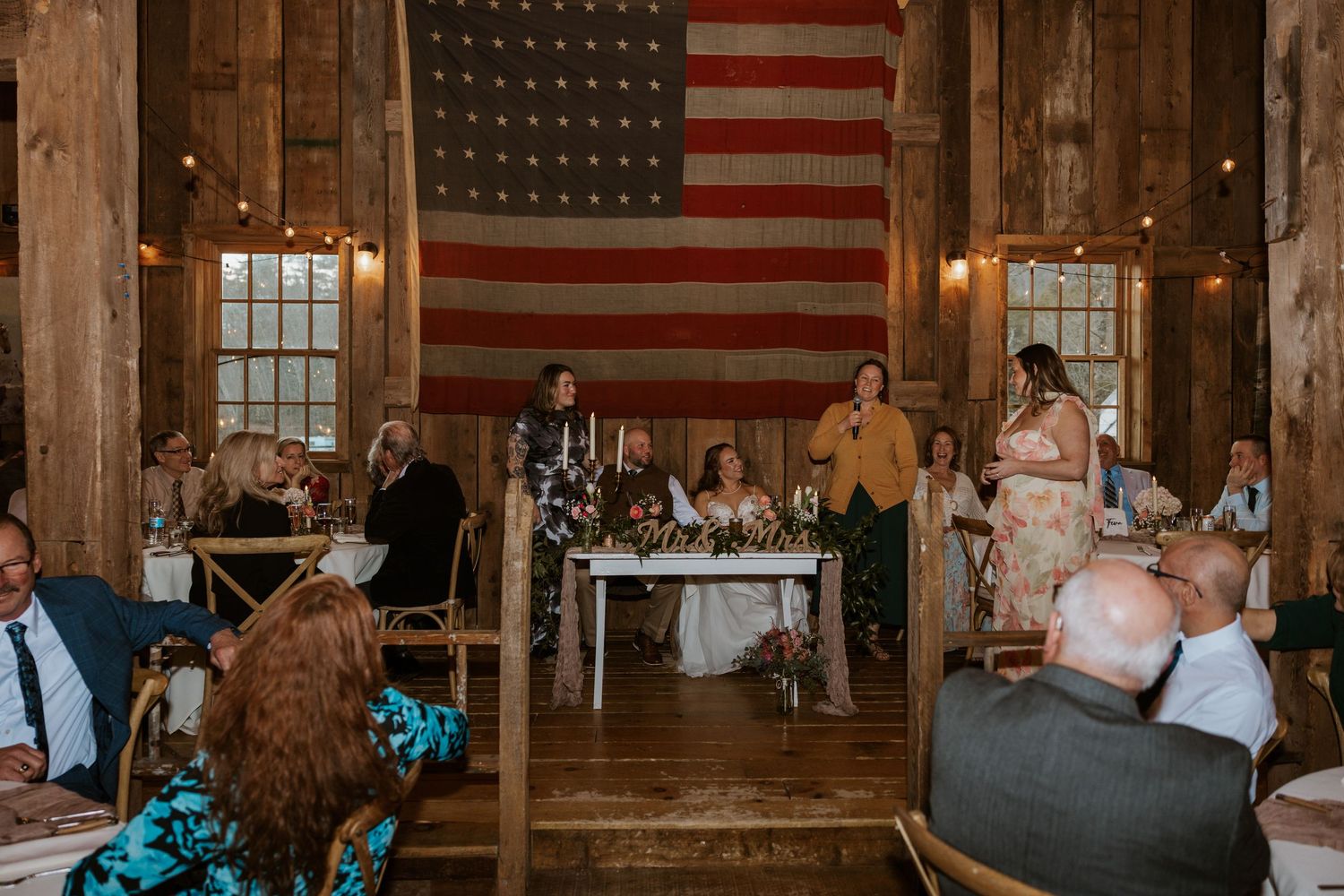 Wedding reception in a rustic barn venue decorated with American flags and wooden beams.