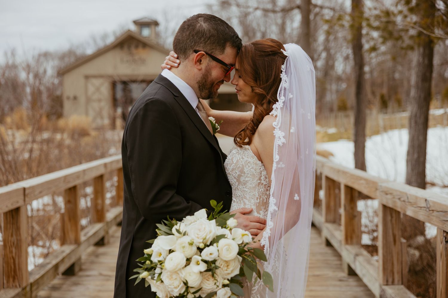 A romantic winter wedding moment on a rustic wooden bridge with a white floral bouquet.