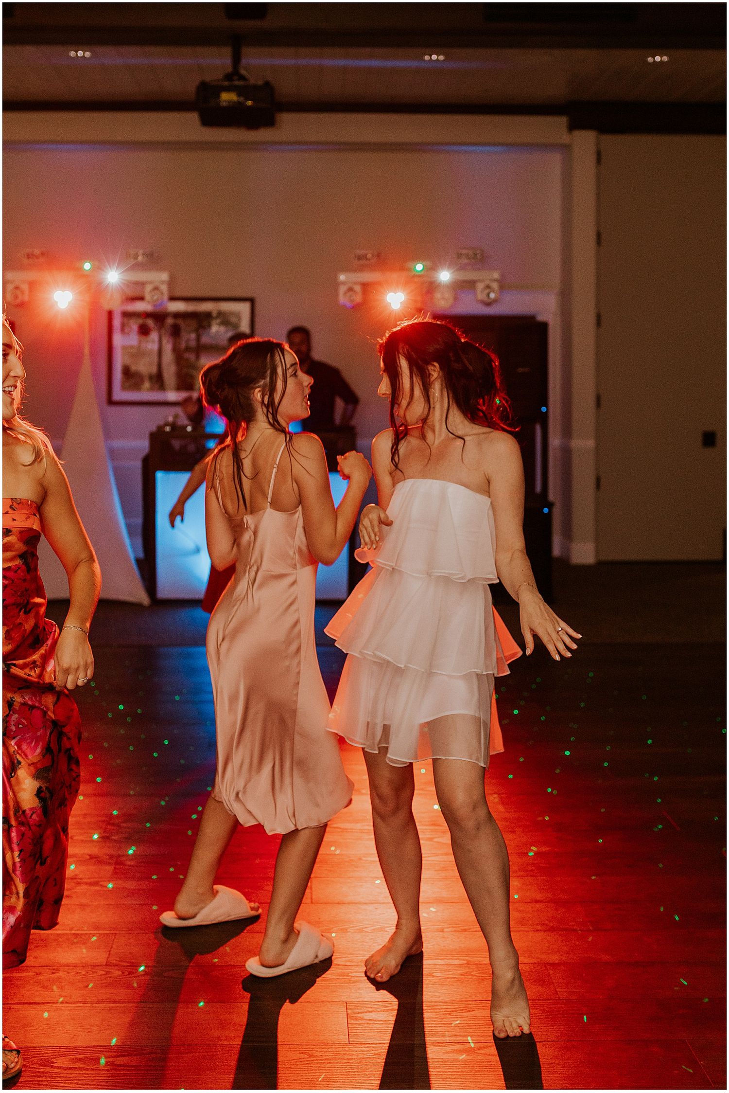 Wedding party dancing in a red-lit reception room with festive atmosphere.