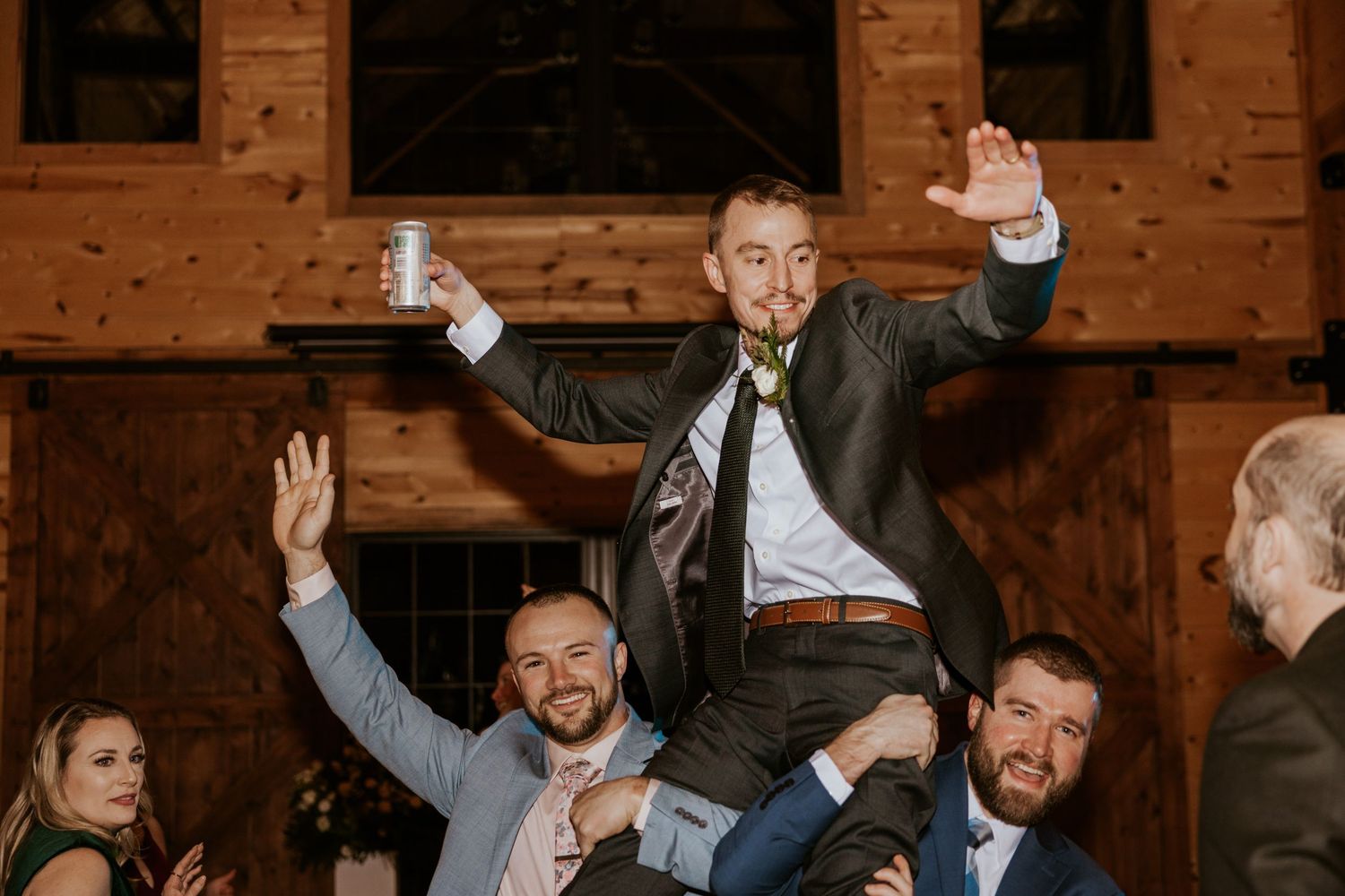 Energetic wedding celebration with guests dancing and raising their hands on a wooden dance floor.