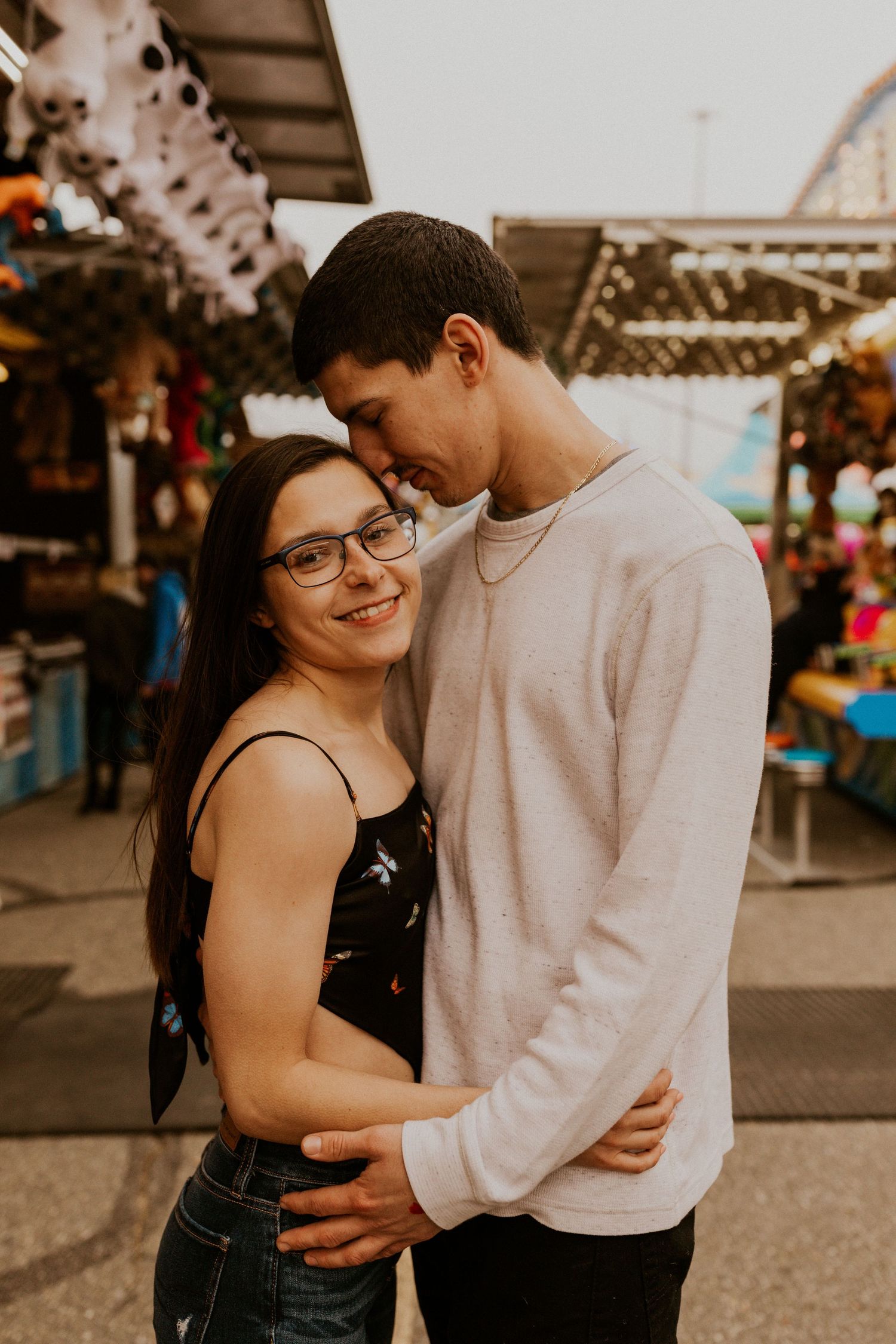Couple embracing at a carnival with amusement rides and festive atmosphere in the background.