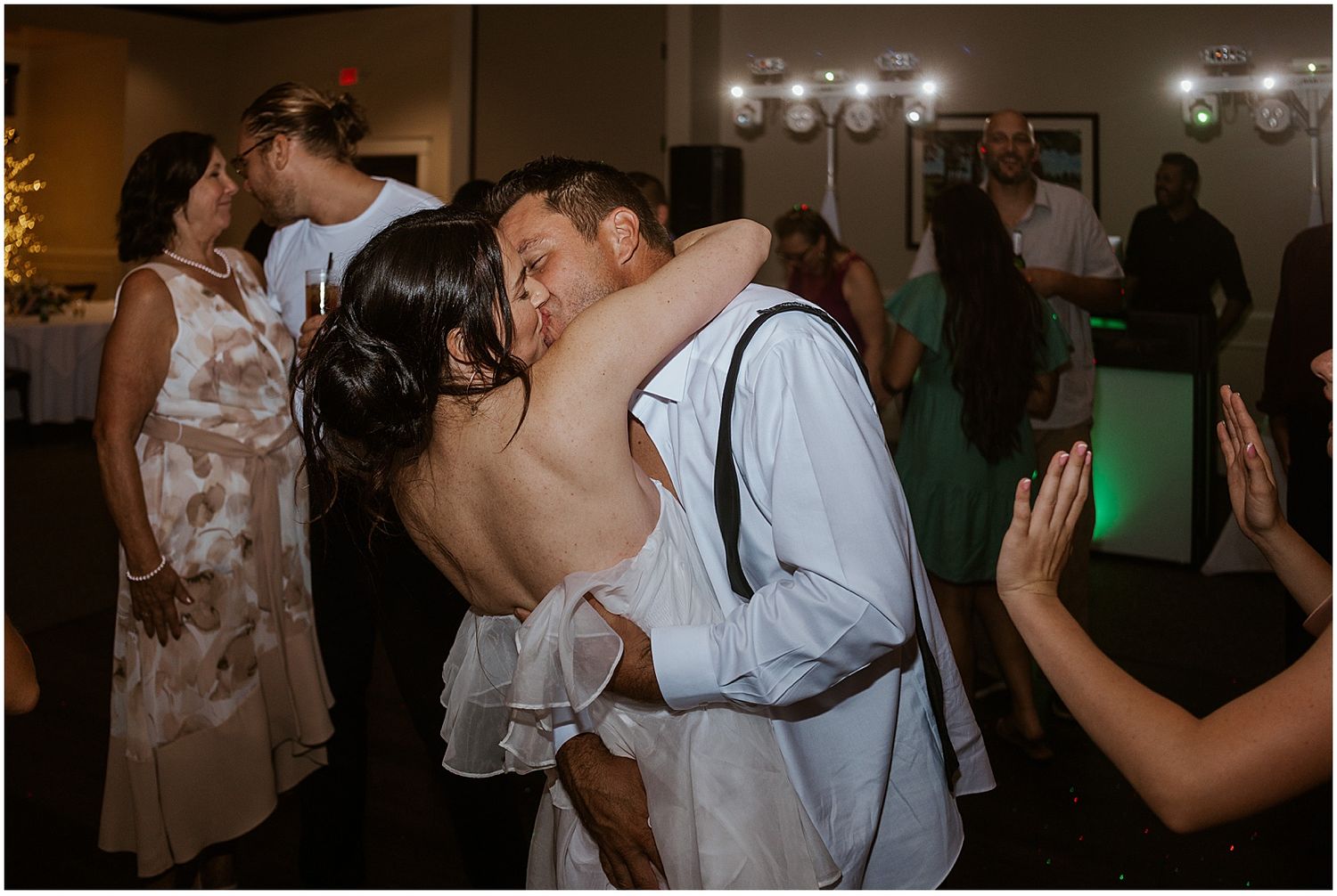 Wedding guests dancing and celebrating on a dimly lit dance floor.