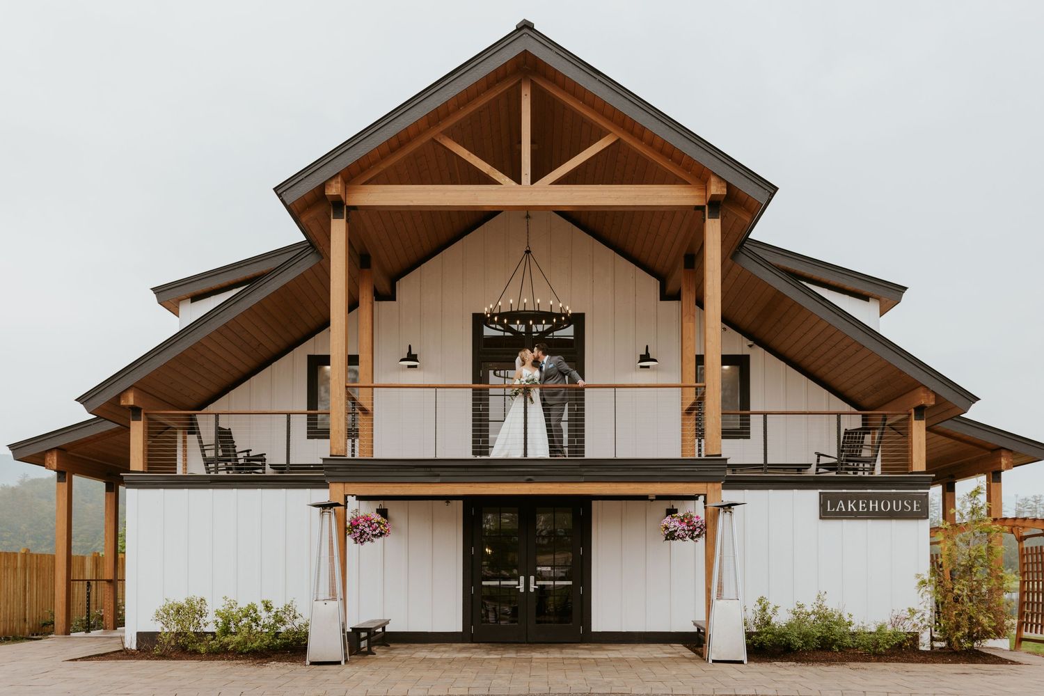 Bride and groom standing on the balcony of a rustic white barn wedding venue called Lakehouse.