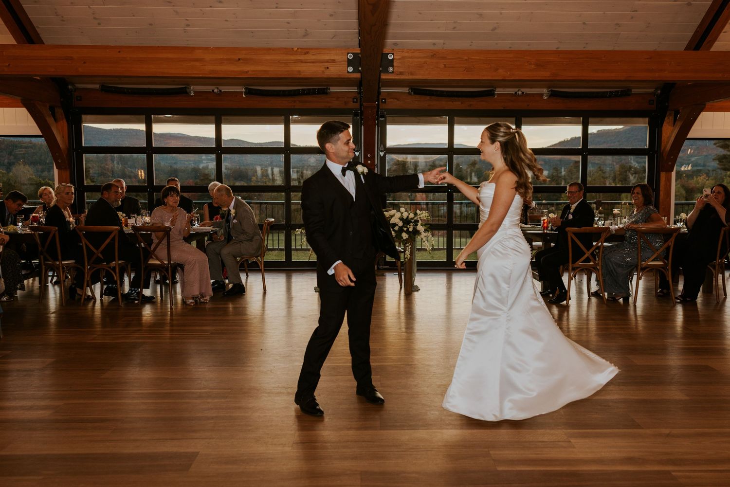 Bride and groom share romantic first dance in elegant reception hall with panoramic windows.