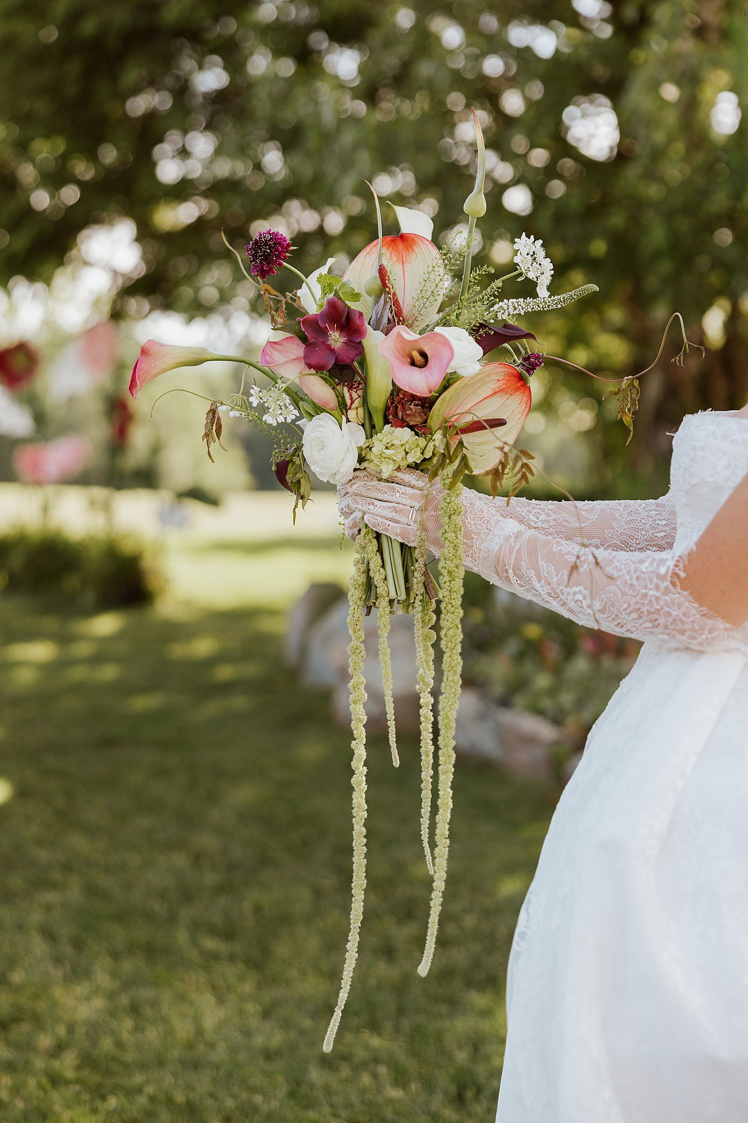 Bride in lace dress holding a lush wedding bouquet with calla lilies and trailing greenery outdoors