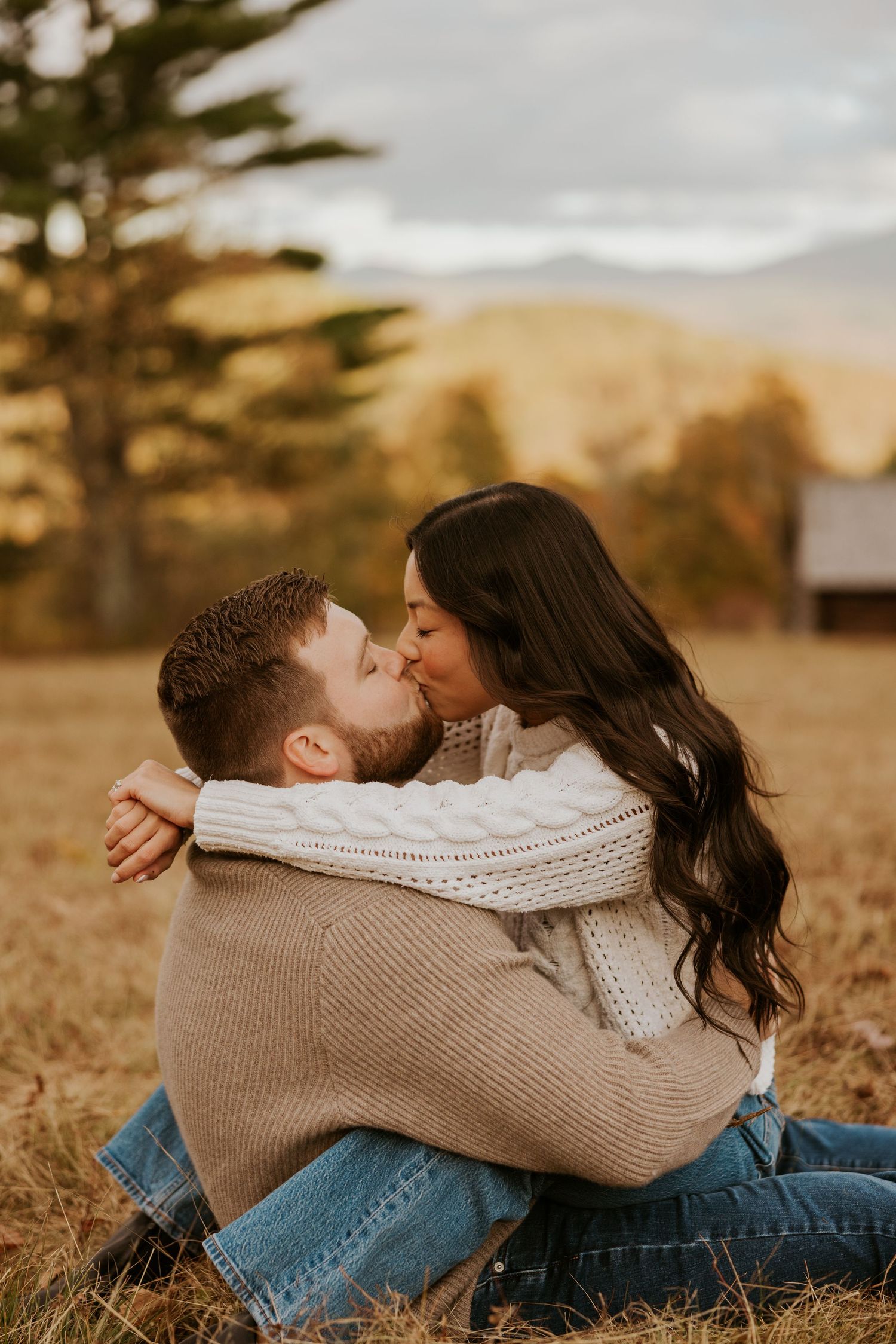 Couple sharing a kiss while sitting together in a golden autumn meadow.