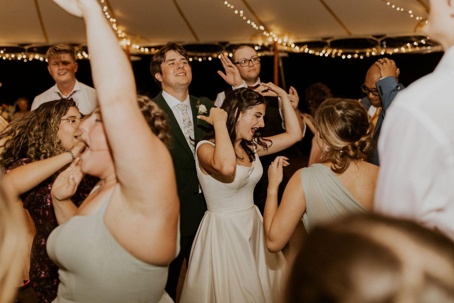 Wedding guests dancing and celebrating at an evening reception under string lights.