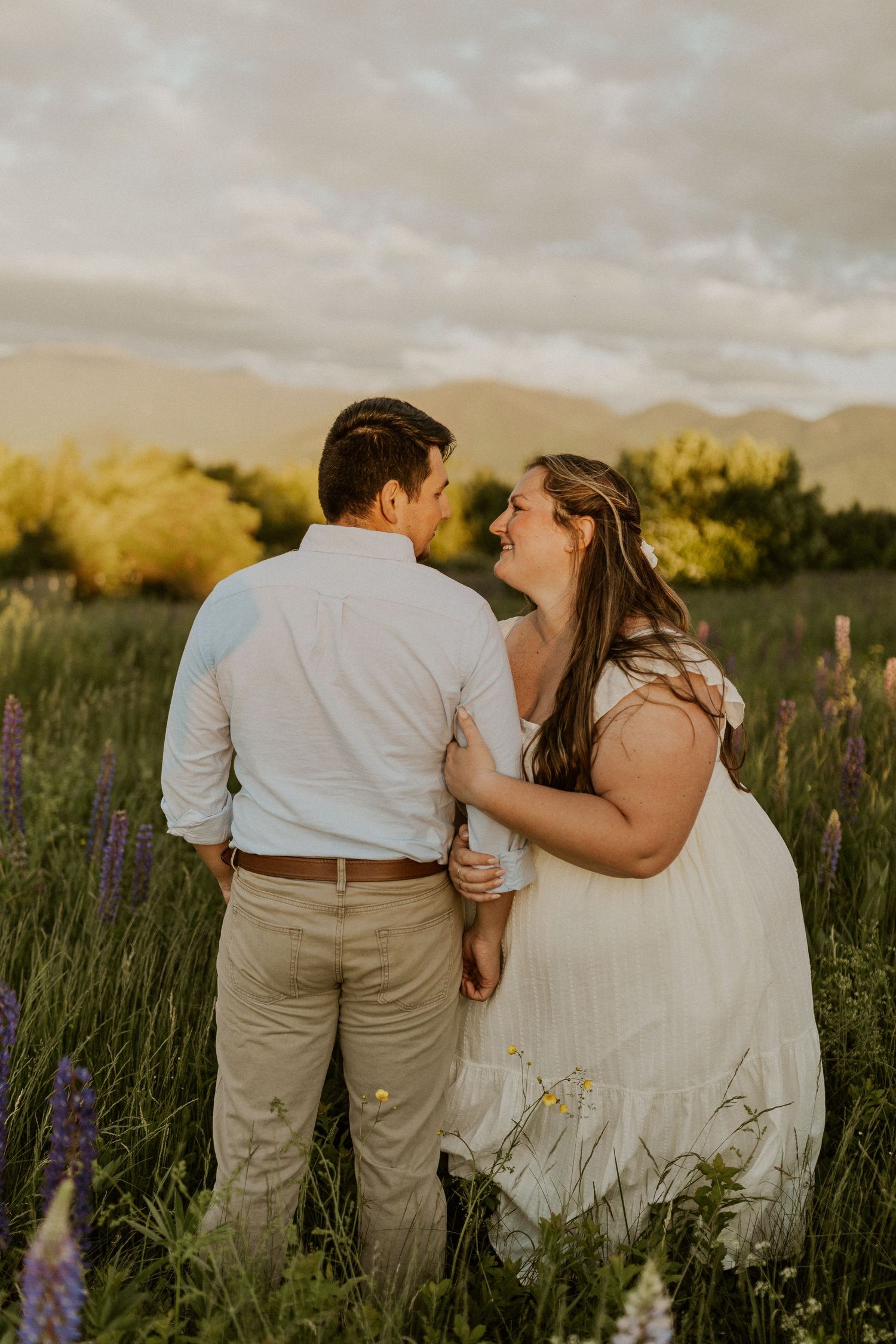 Terise hugging onto Jose's arm and smiling during an engagement photoshoot in the lupine fields of Sugar Hill NH.