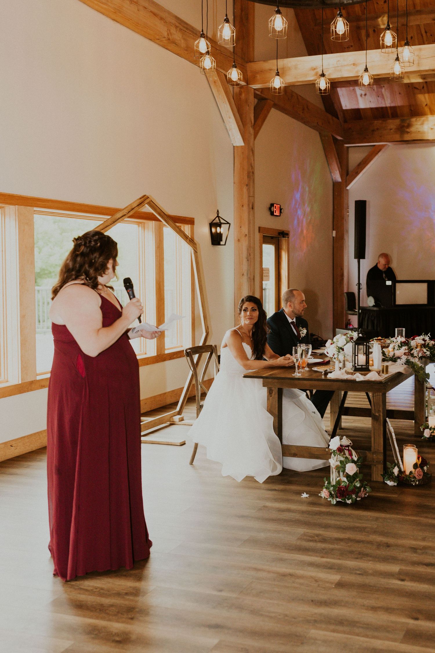 Wedding celebration in a barn-style venue with burgundy-clad attendants and white decor.
