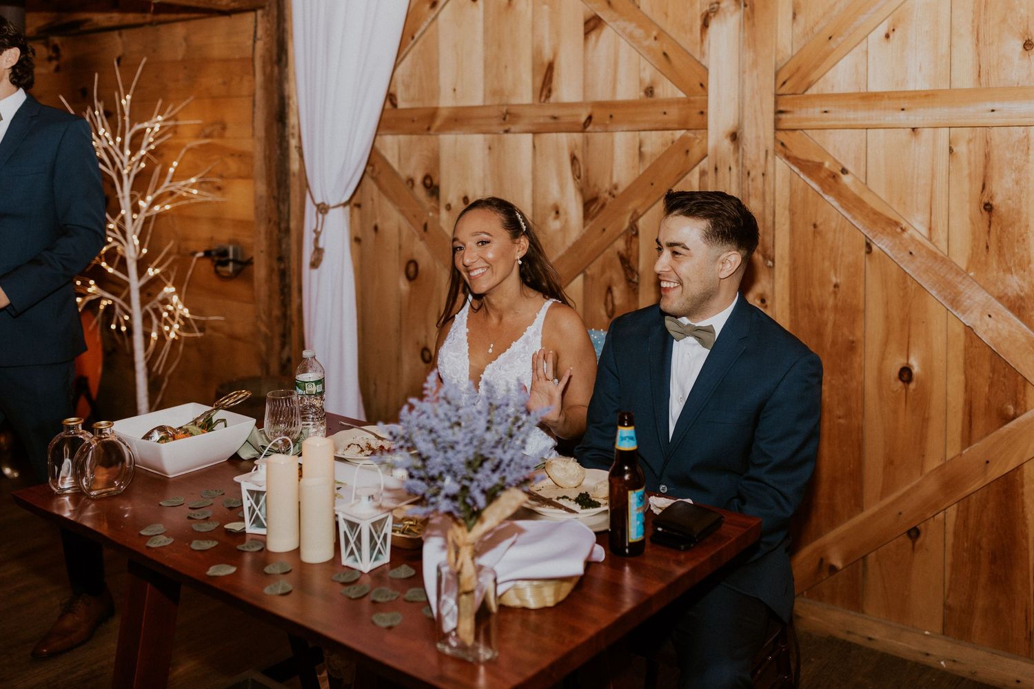 Intimate dinner setting in a wooden barn with decorative branches and white table settings.