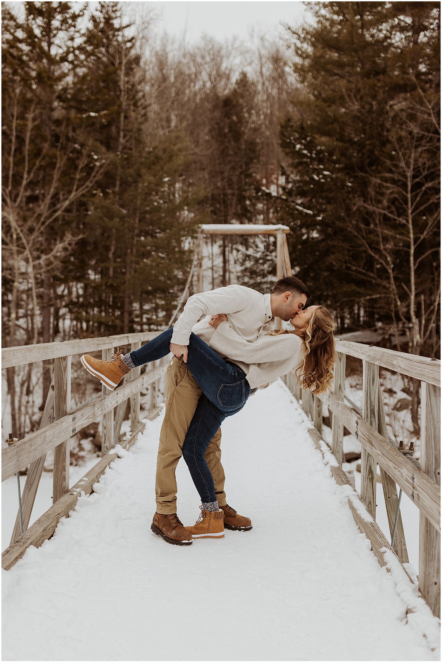 Romantic dip pose on a snowy bridge surrounded by winter forest.