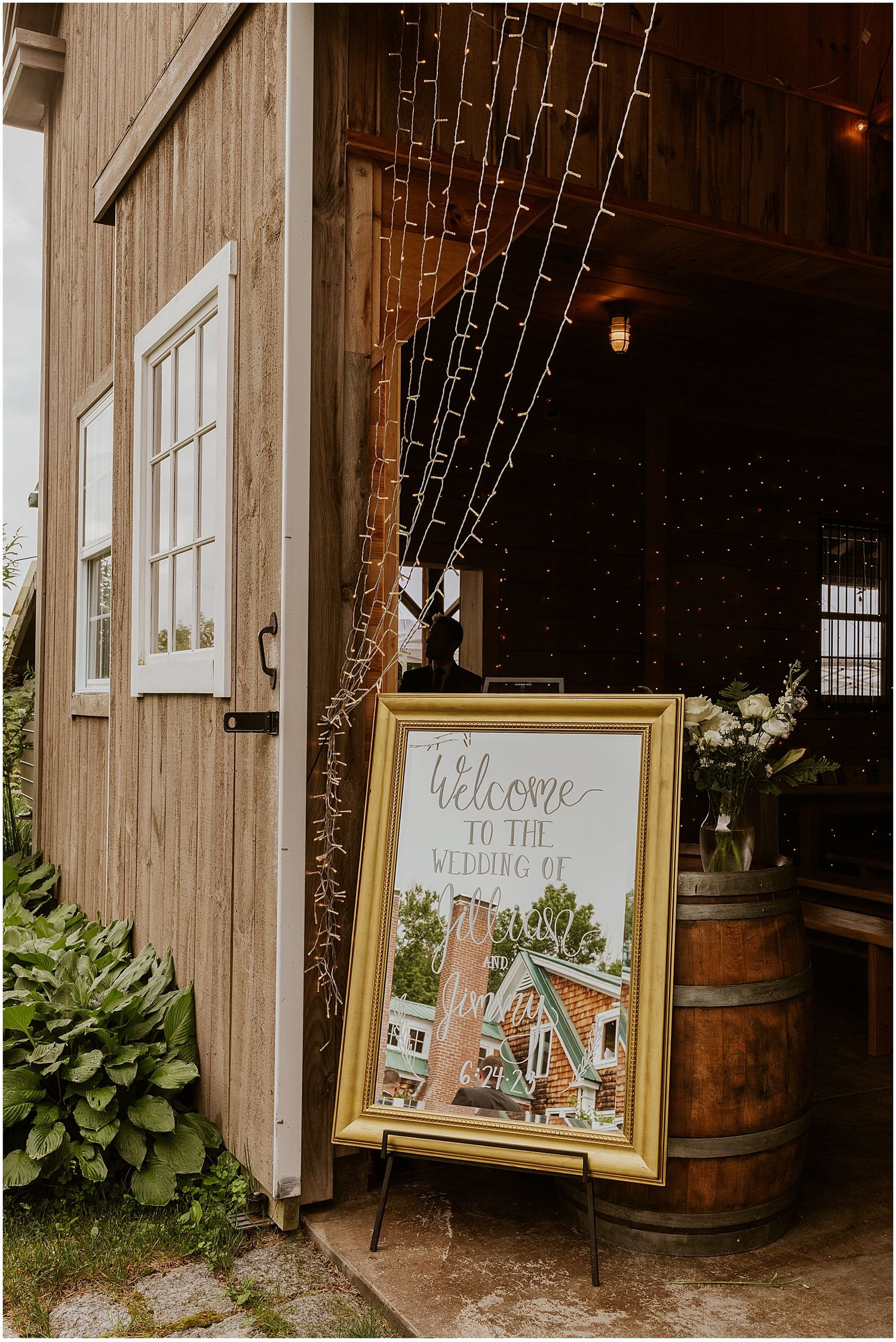 Rustic barn entrance decorated with string lights and welcome signs in gold frames.