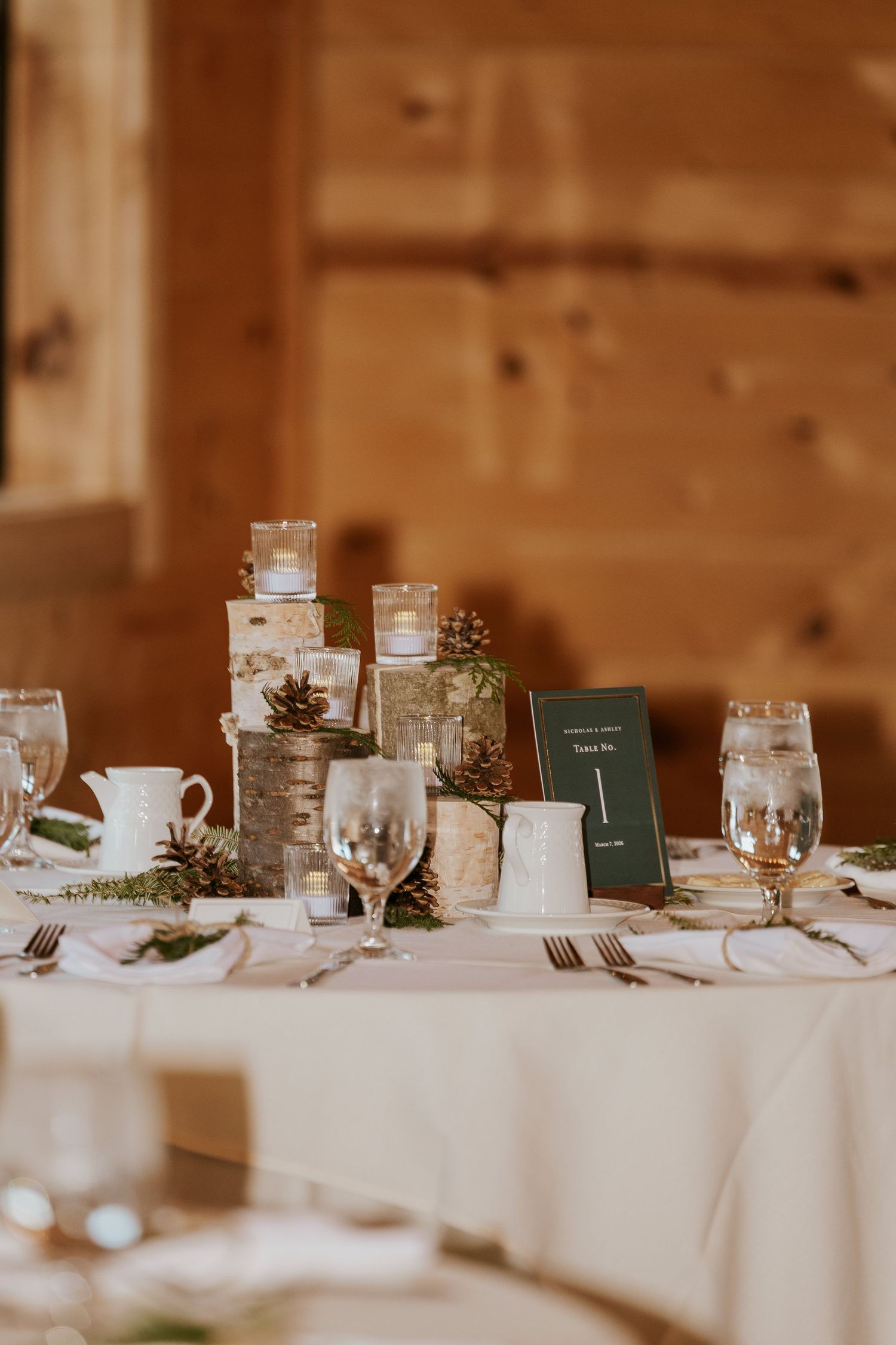 Elegant table setting with birch log centerpieces and green table numbers in a rustic venue.