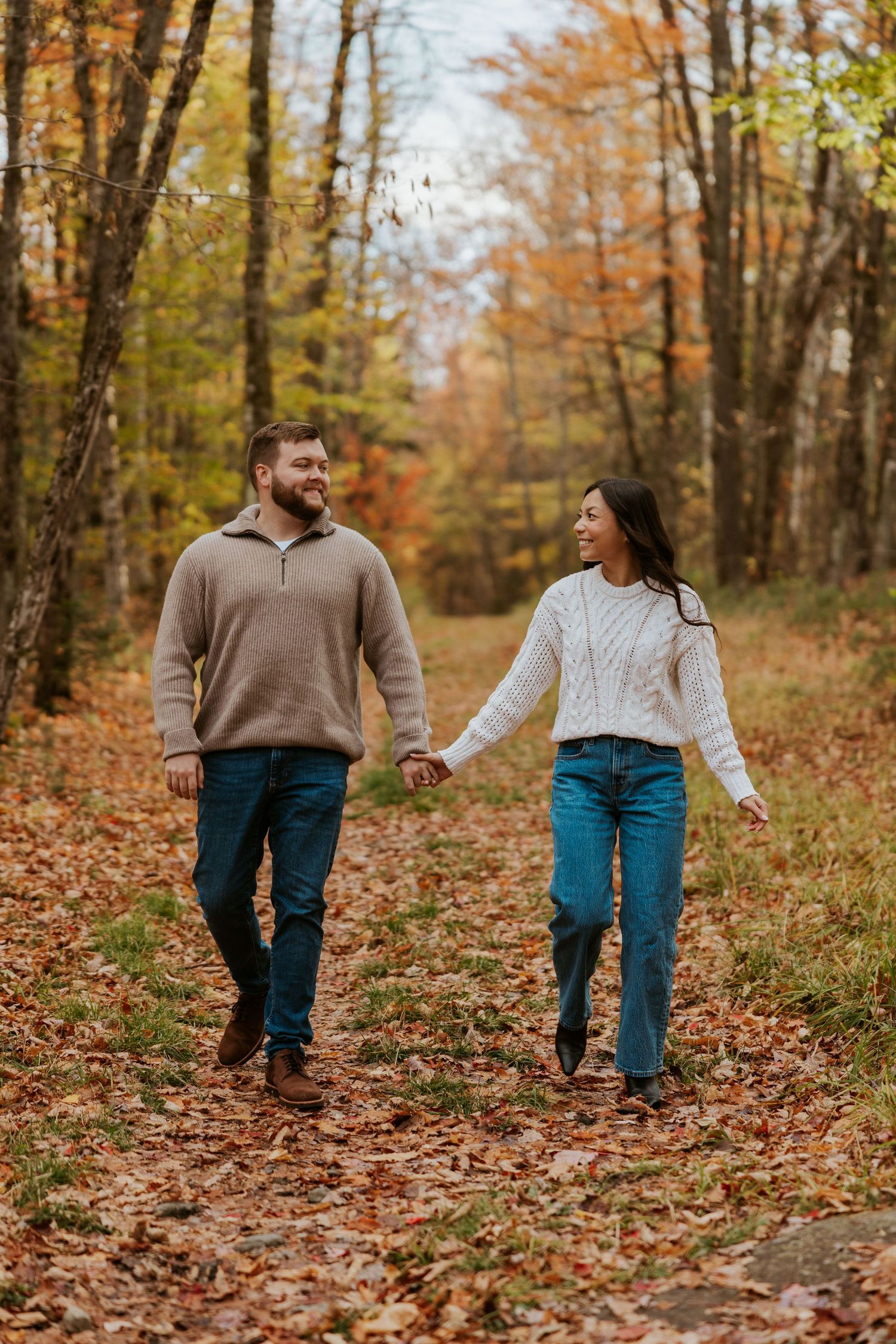 Happy couple holding hands walking through a colorful autumn forest path.
