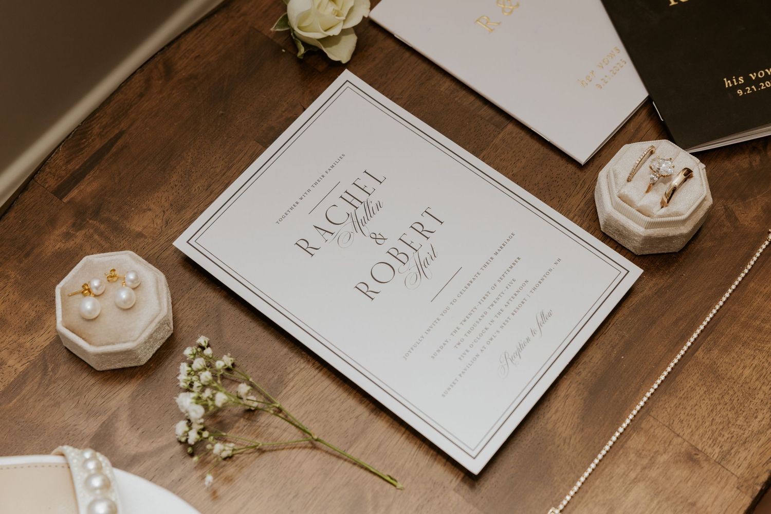 Classic black and white wedding invitation for Rachel and Robert displayed on a wooden table with pearl earrings.
