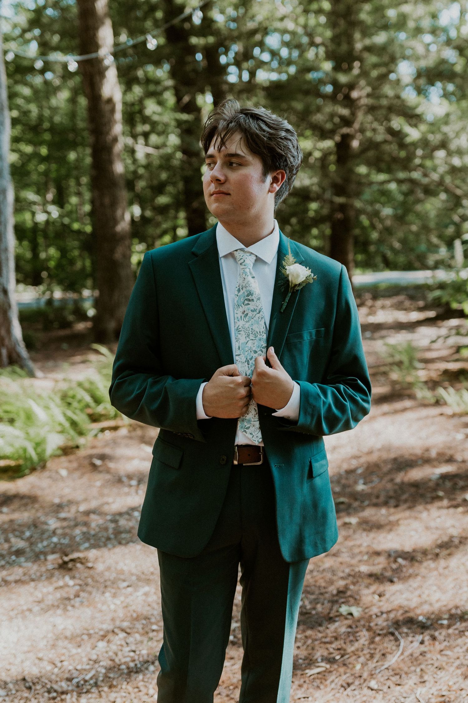 Wedding party members in emerald green suits standing in a wooded outdoor setting.
