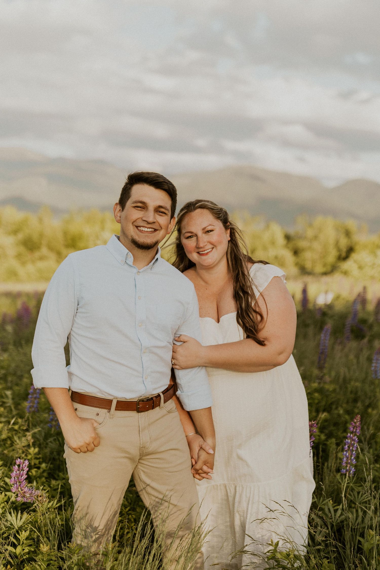Terise hugging onto Jose's arm and smiling during an engagement photoshoot in the lupine fields of Sugar Hill NH.