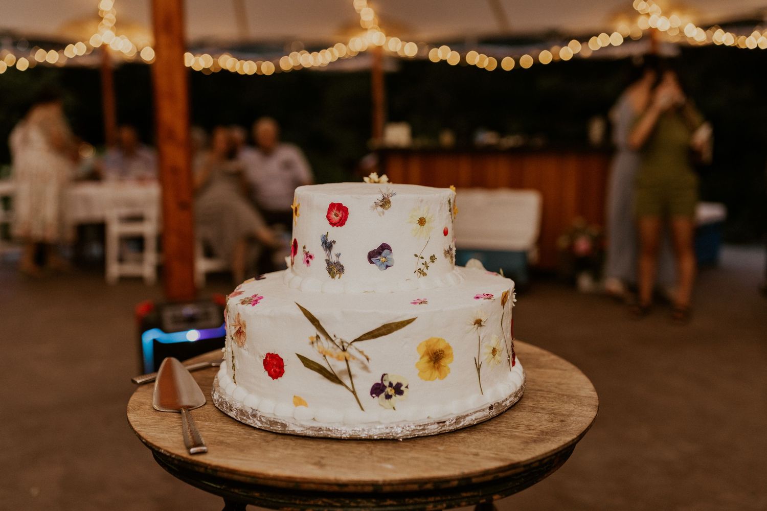 White wedding cake with delicate floral decorations displayed on a rustic wooden stand.
