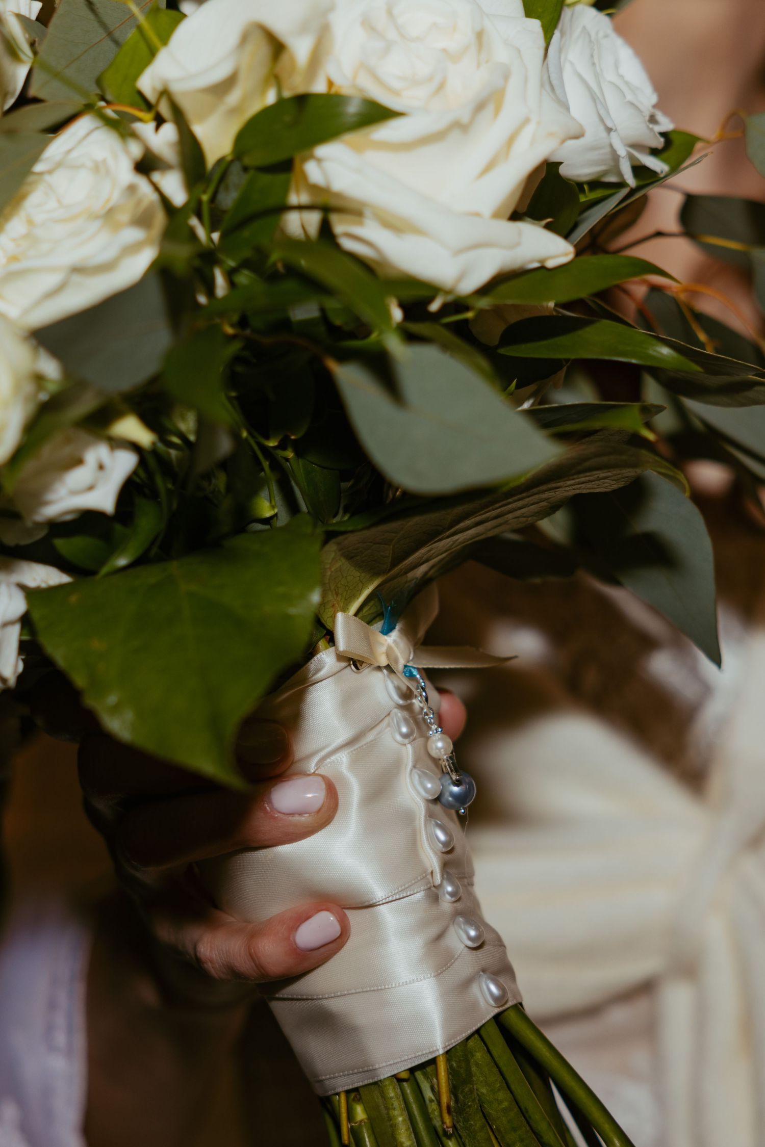 White roses in a bridal bouquet decorated with delicate blue butterfly charms and wrapped in satin ribbon.