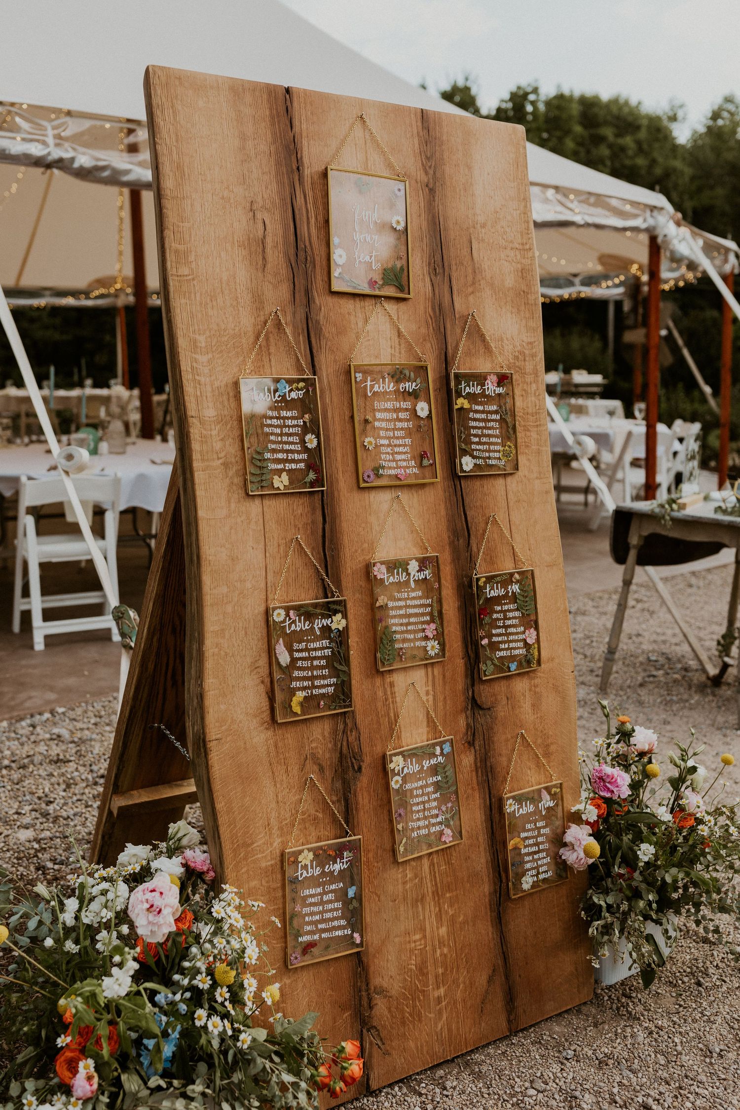 Wooden seating chart display with handwritten signs and fresh flowers.