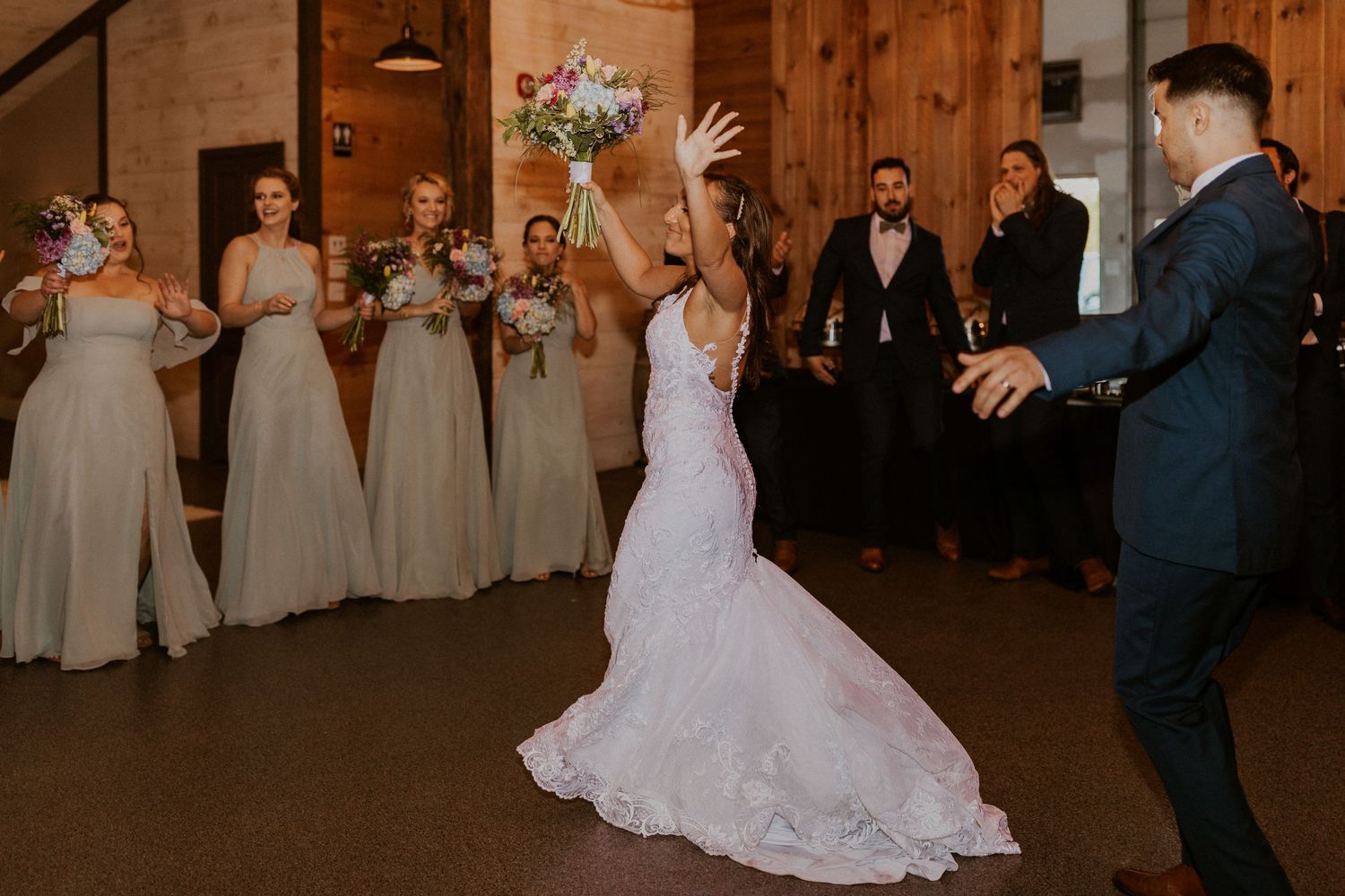 Wedding couple dances together in a barn venue with wood paneled walls and warm lighting.