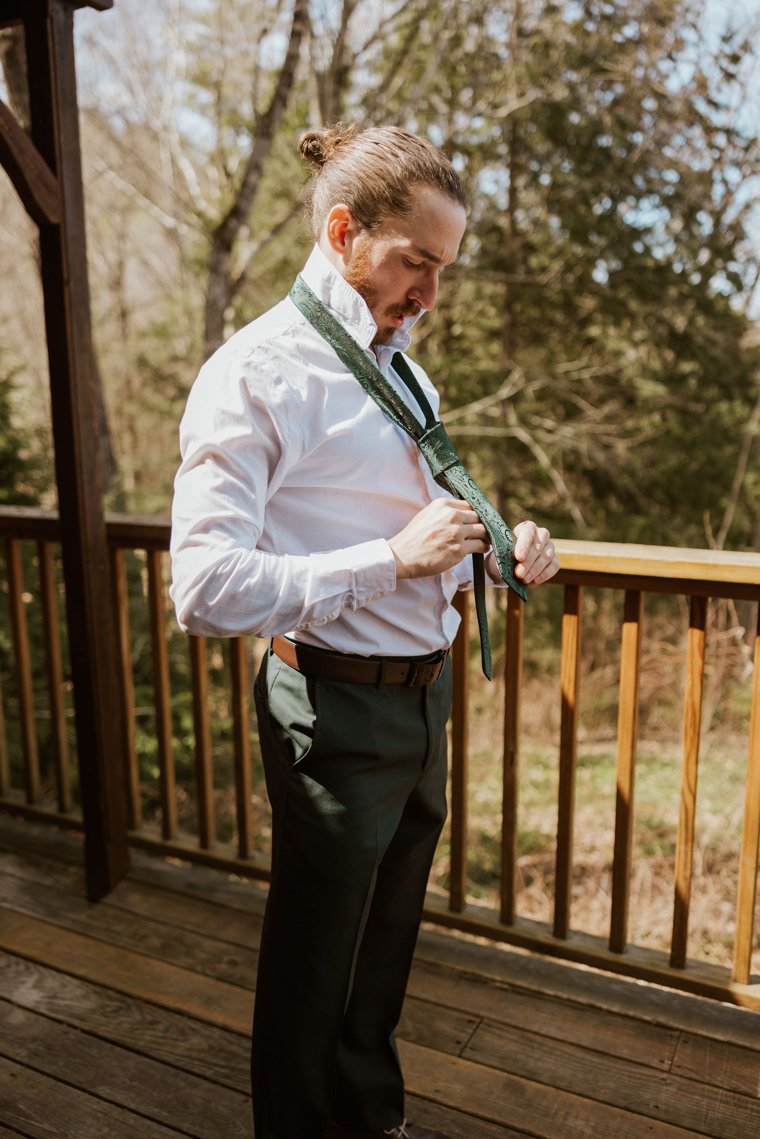 Groom adjusting green tie on outdoor deck while getting ready for wedding ceremony.