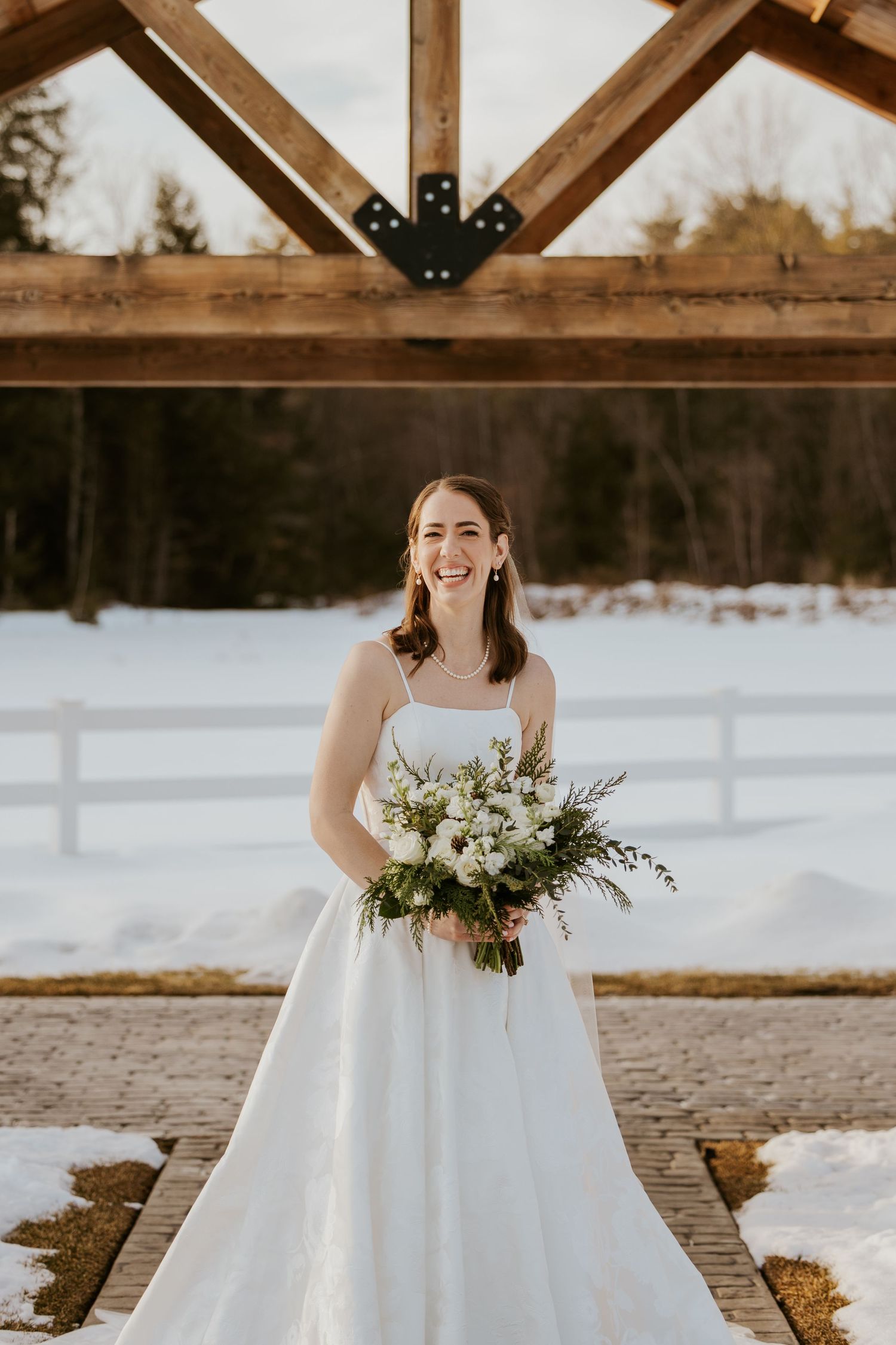 Bride in a white ballgown poses for portraits in front of a snowy winter landscape with wooden beams.
