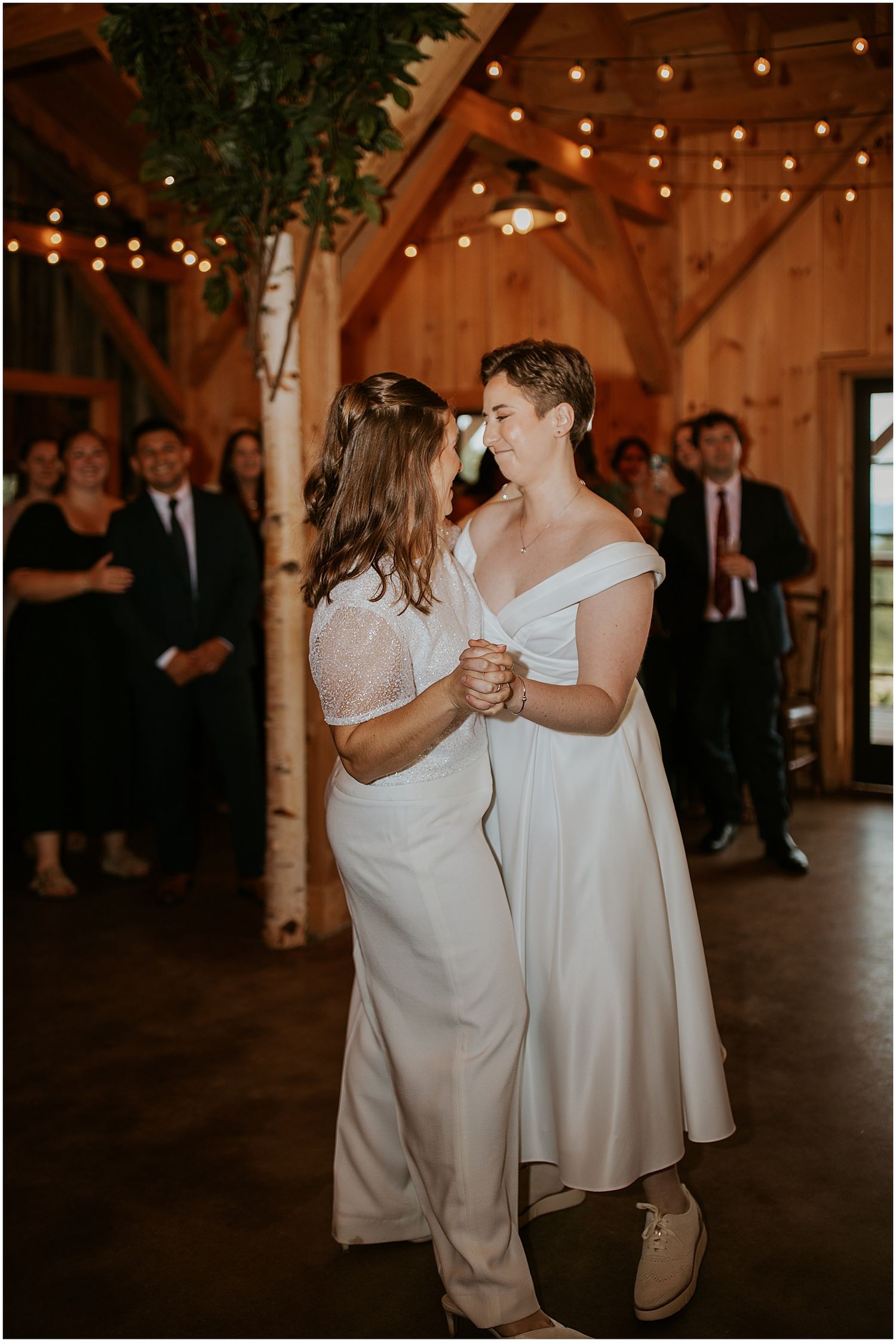 Couples dancing together in an intimate rustic barn venue with string lights and birch trees.