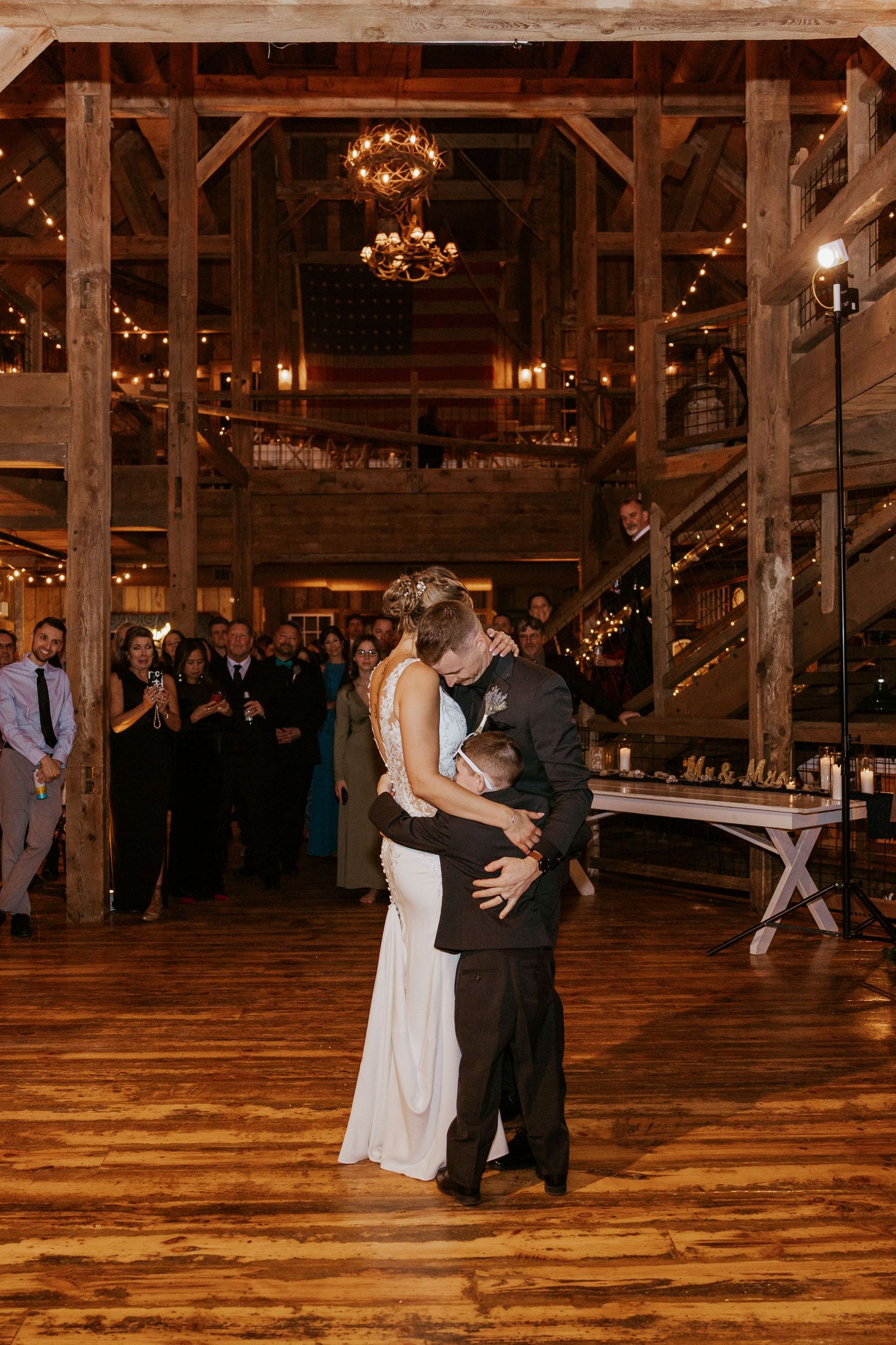 Bride and groom share their first dance in a rustic barn wedding venue with warm string lights and wood beams.